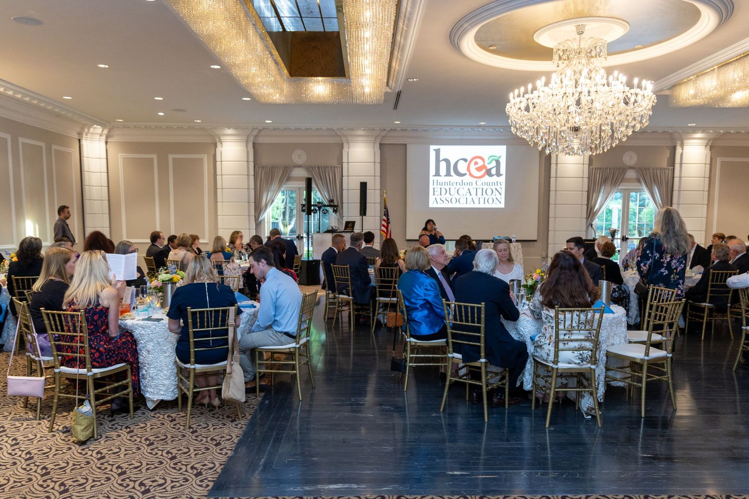 Conference attendees gathered in an elegant ballroom with crystal chandeliers for a corporate presentation or meeting.