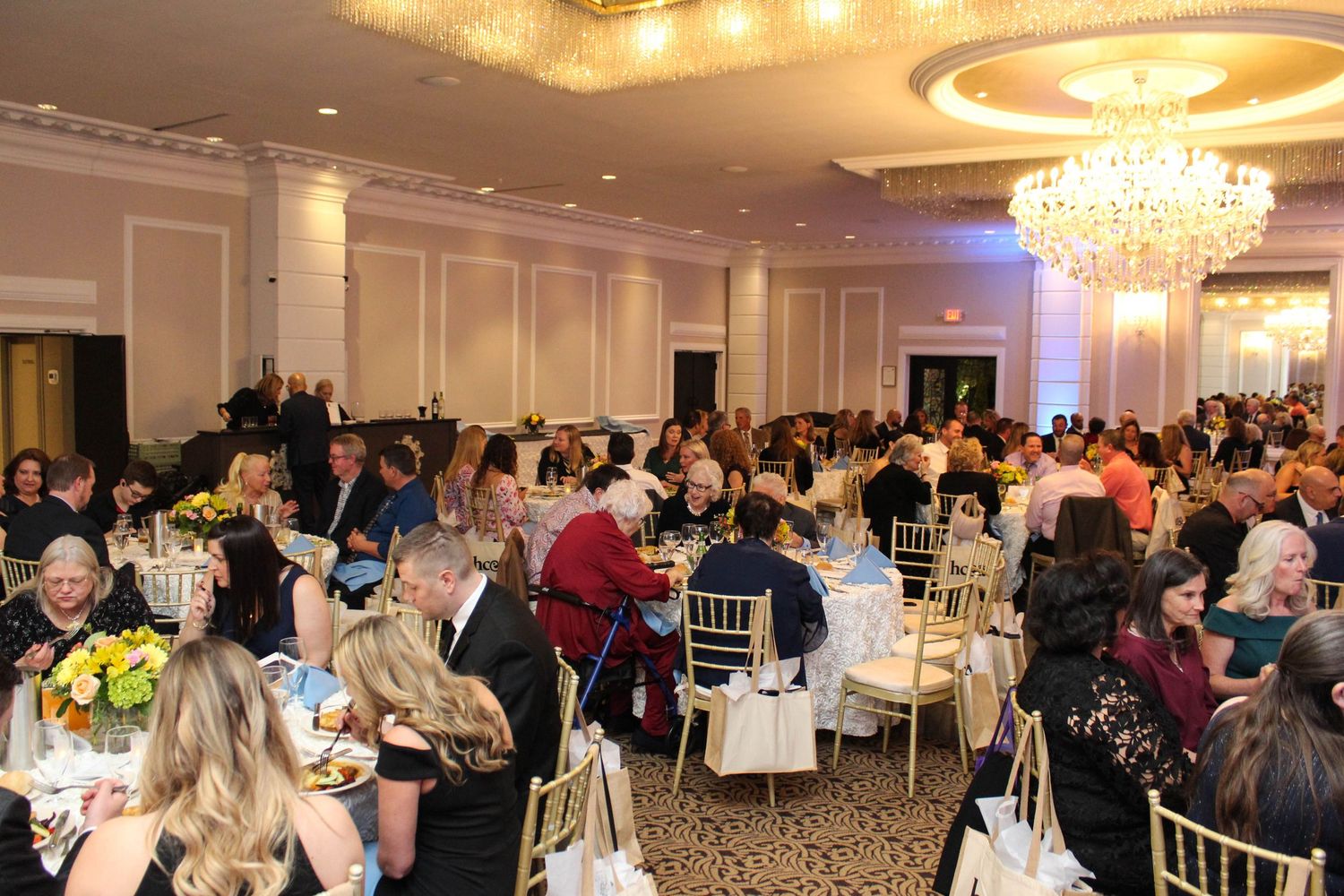 Elegant banquet hall filled with guests seated at round tables under crystal chandeliers.