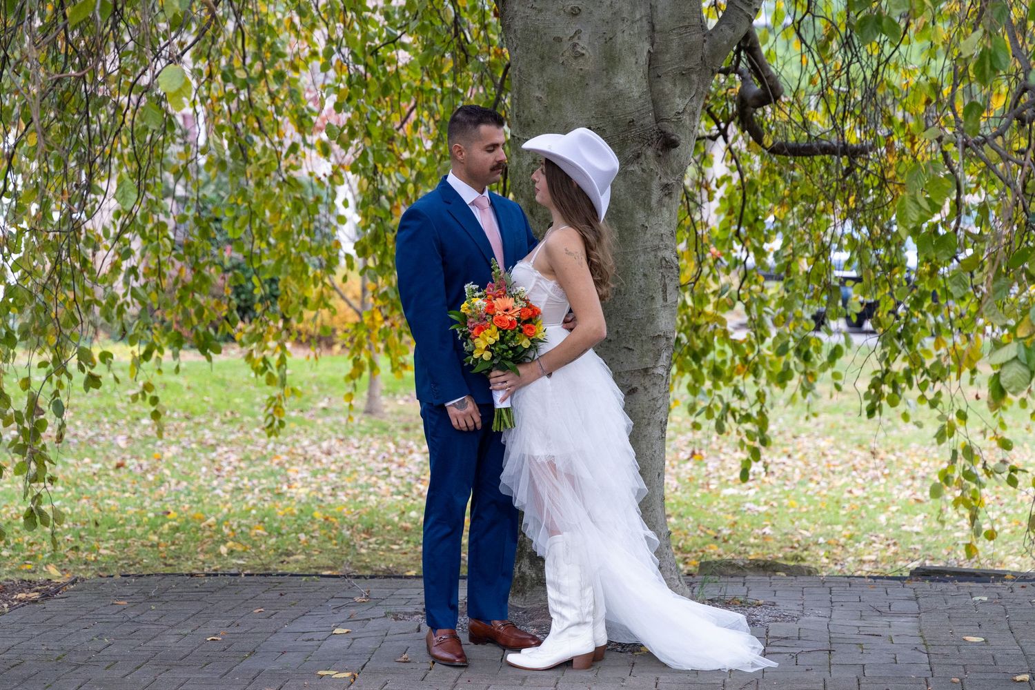 A romantic couple shares an intimate moment under a weeping willow tree during their outdoor wedding celebration.
