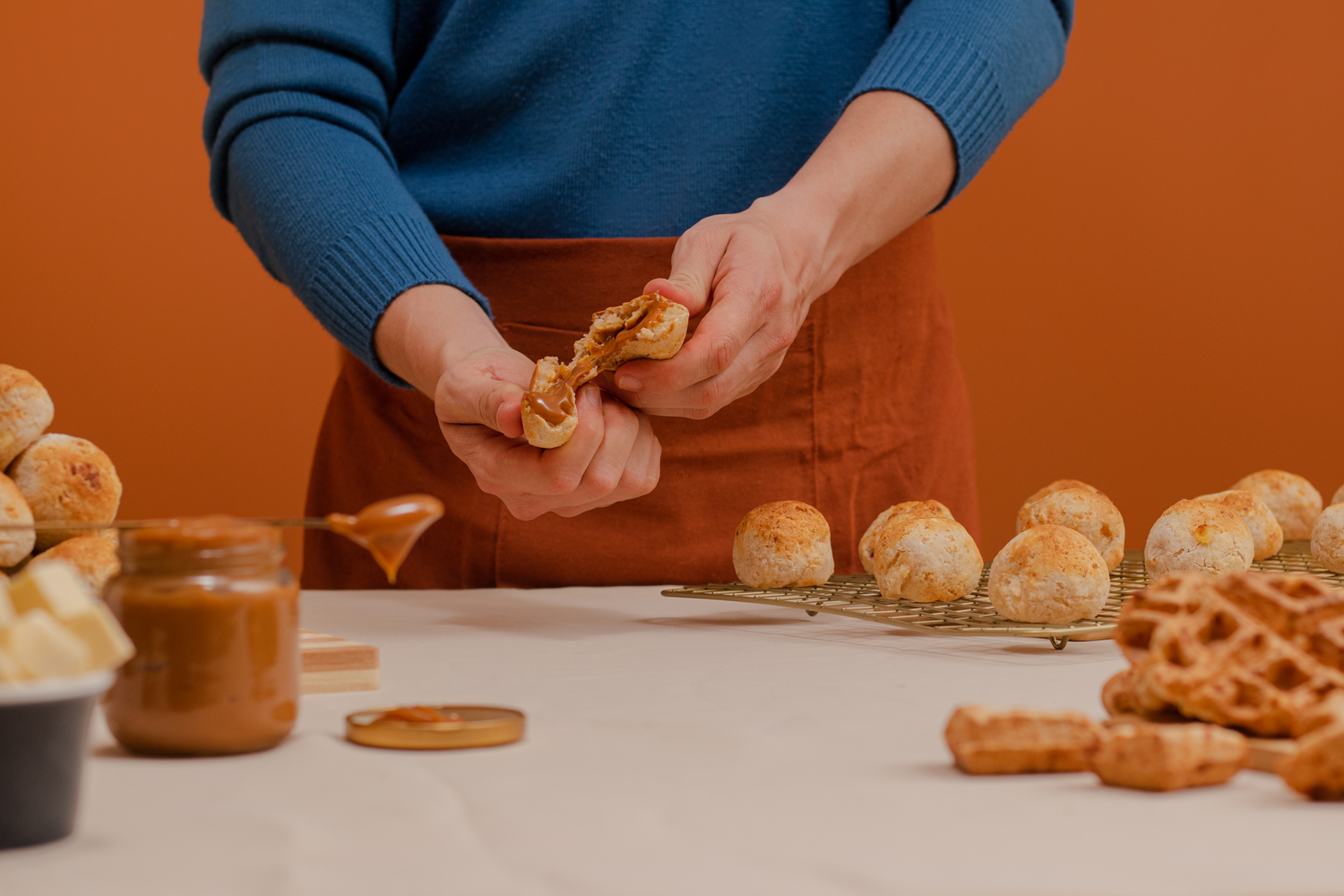 Hands in a blue sweater prepare snacks on a white counter with pretzels and bread rolls scattered about.