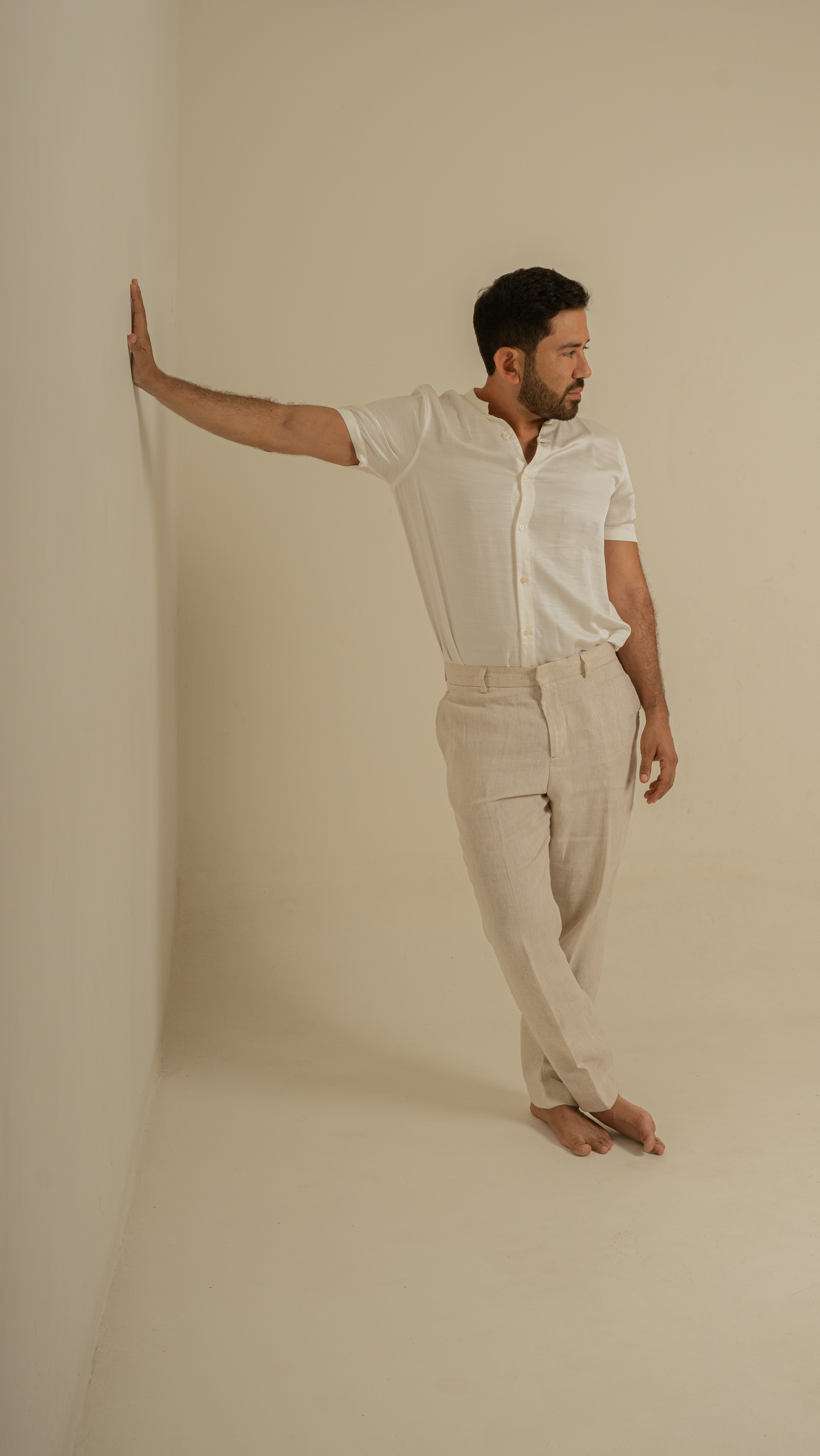 Minimalist fashion photo of person in all-white outfit against beige wall with dramatic pose.
