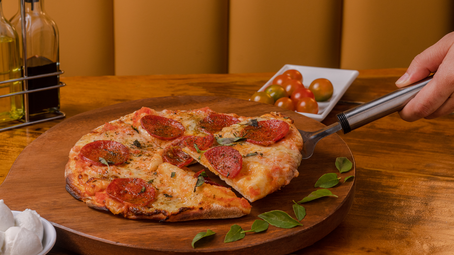 Pizza being cut with scissors on wooden serving board with fresh herbs.