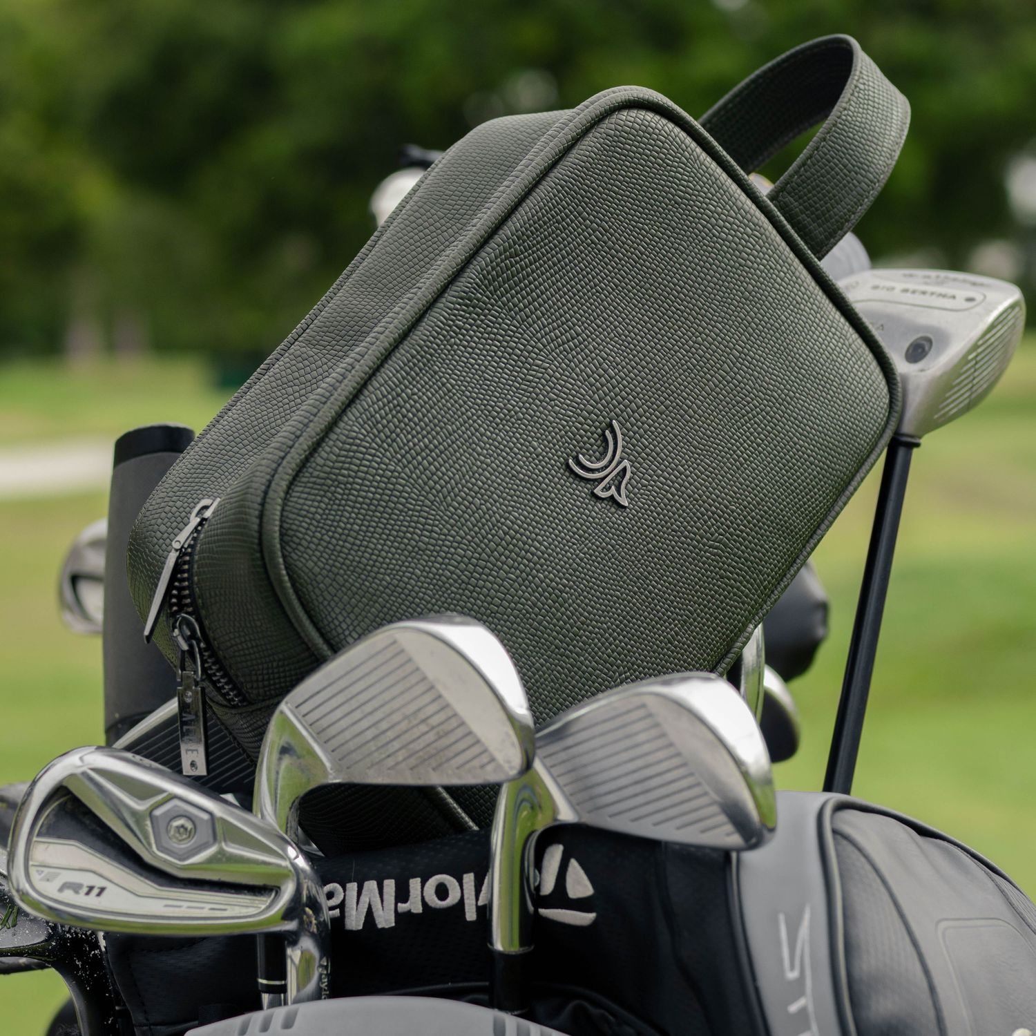 Green leather golf accessory bag showcasing golf clubs against outdoor course background.