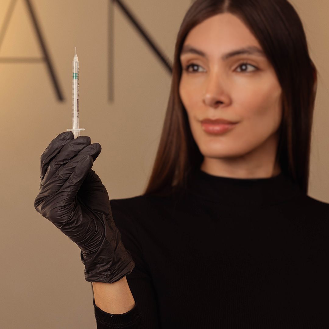 Professional medical setting with black gloved hand holding syringe against ANTI signage.