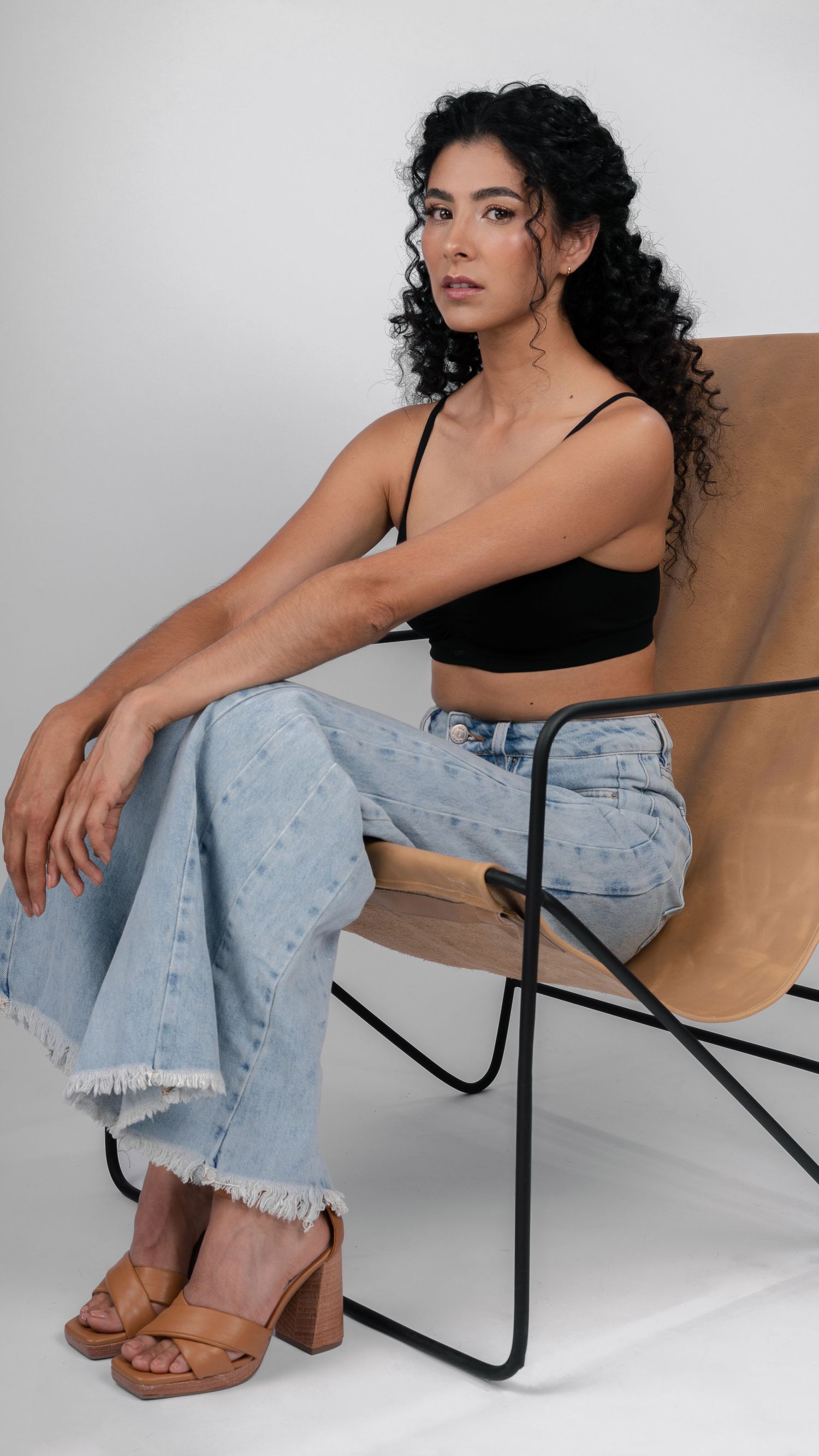 Stylish portrait with curly hair wearing black top and distressed denim in minimalist setting.