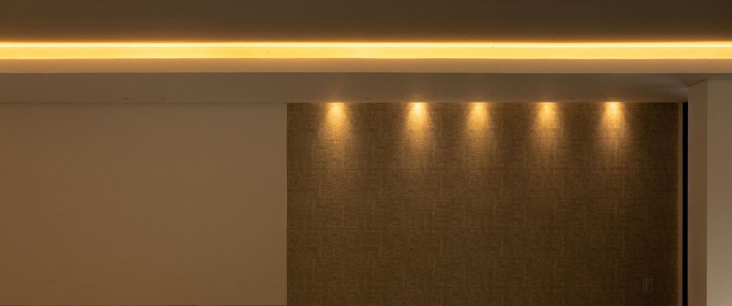 Modern interior ceiling with warm LED strip lighting and recessed spotlights illuminating a textured wall panel.