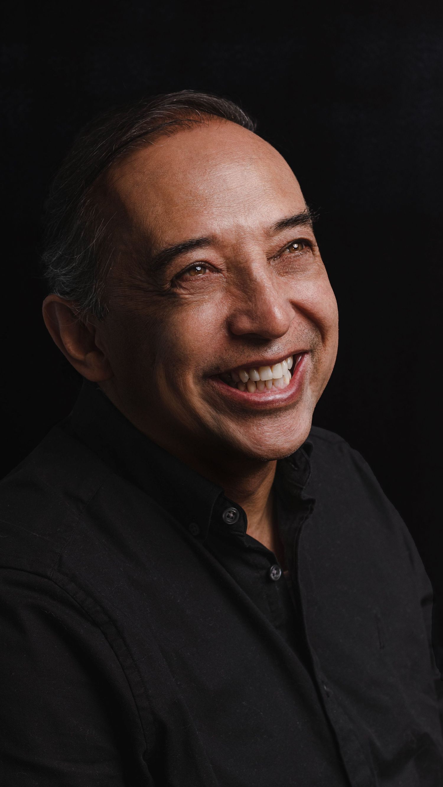 Candid portrait of a person laughing against a dark background.