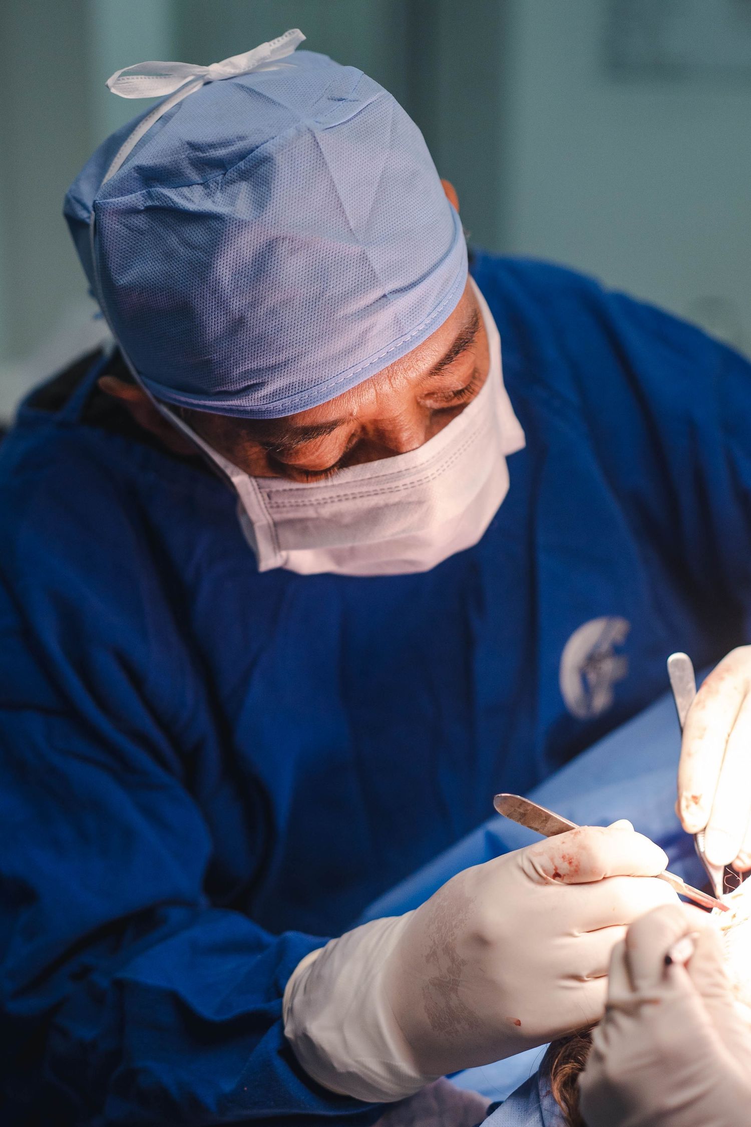 Surgeon in blue scrubs and mask performing delicate medical procedure.