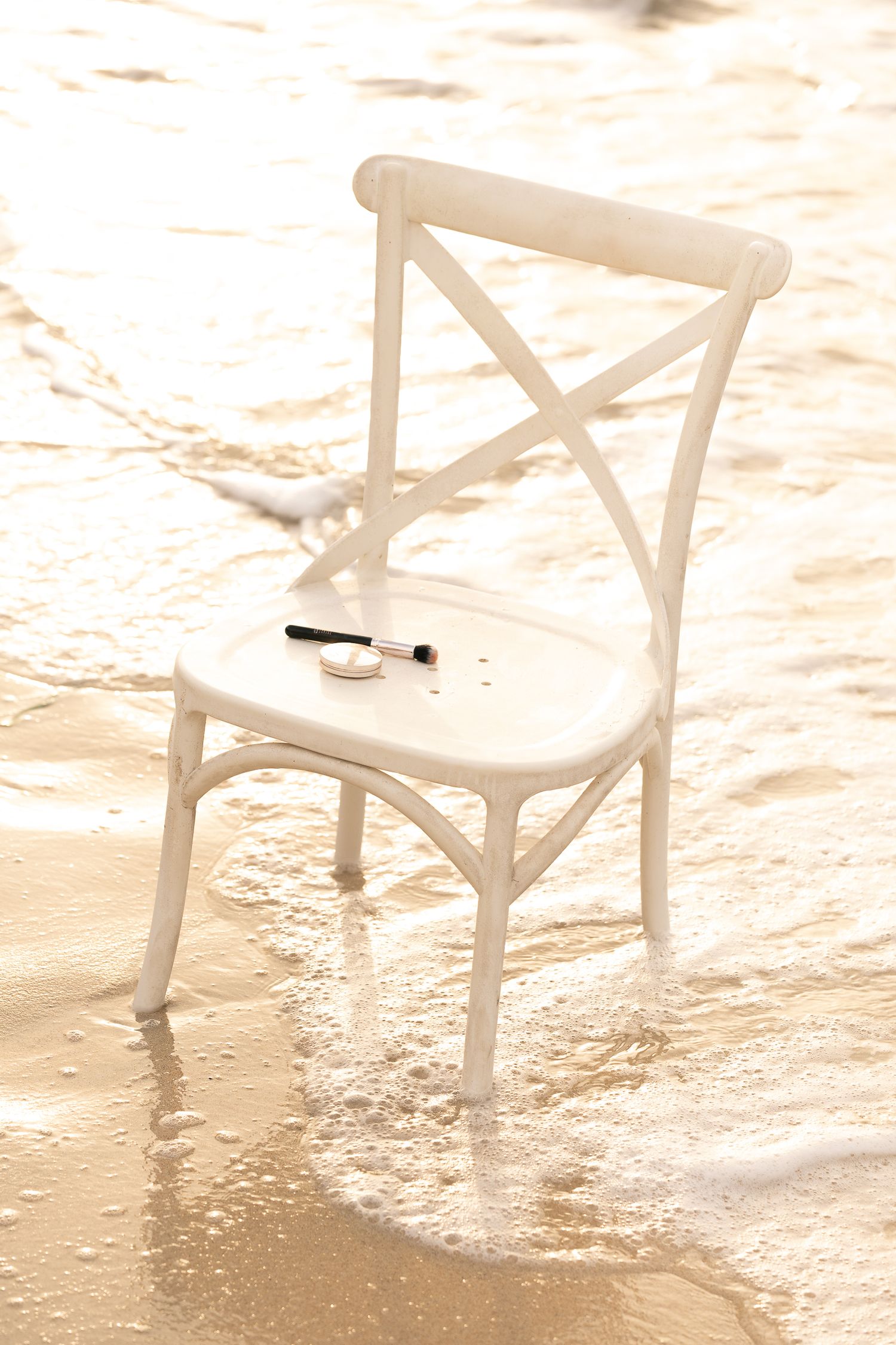 White wooden chairs arranged artistically on wet sandy beach during golden hour.