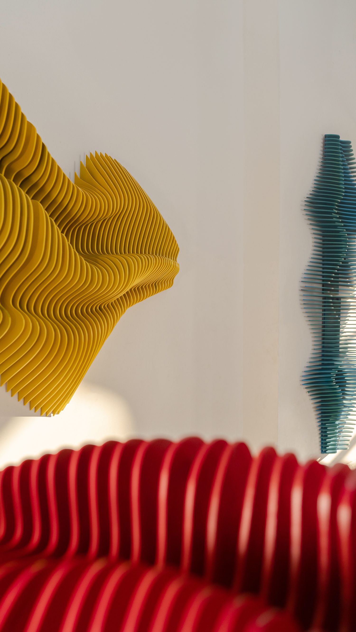 Abstract art installation featuring wavy patterns in yellow, red and teal against a white wall.