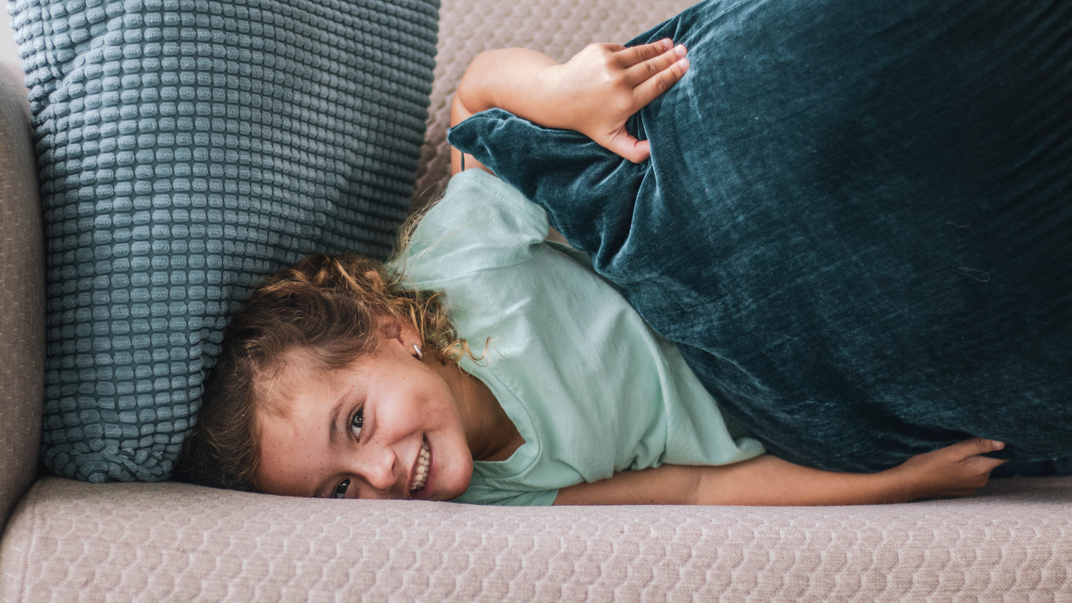 Child laying on grey couch laughing during casual moment.