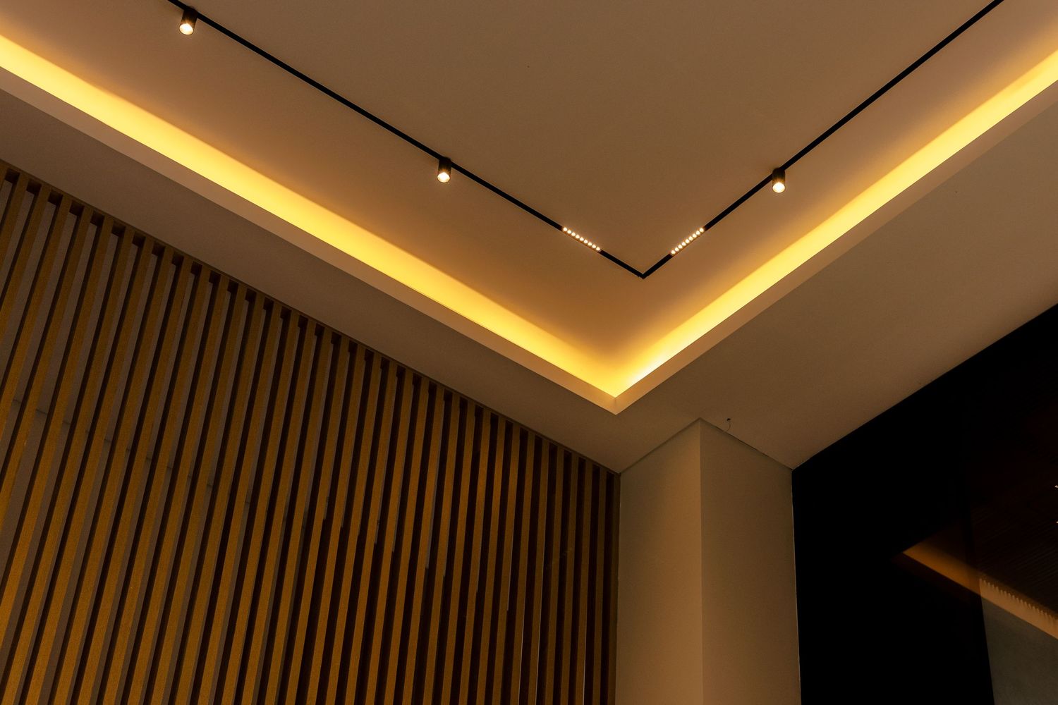 Modern ceiling with warm LED strip lighting and recessed spotlights above elegant wood slat wall panels.