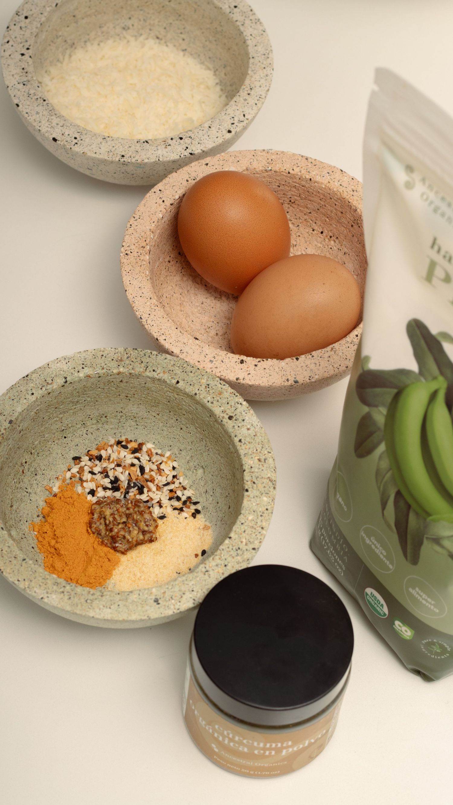 Overhead view of cooking ingredients with eggs and spices in stone bowls.
