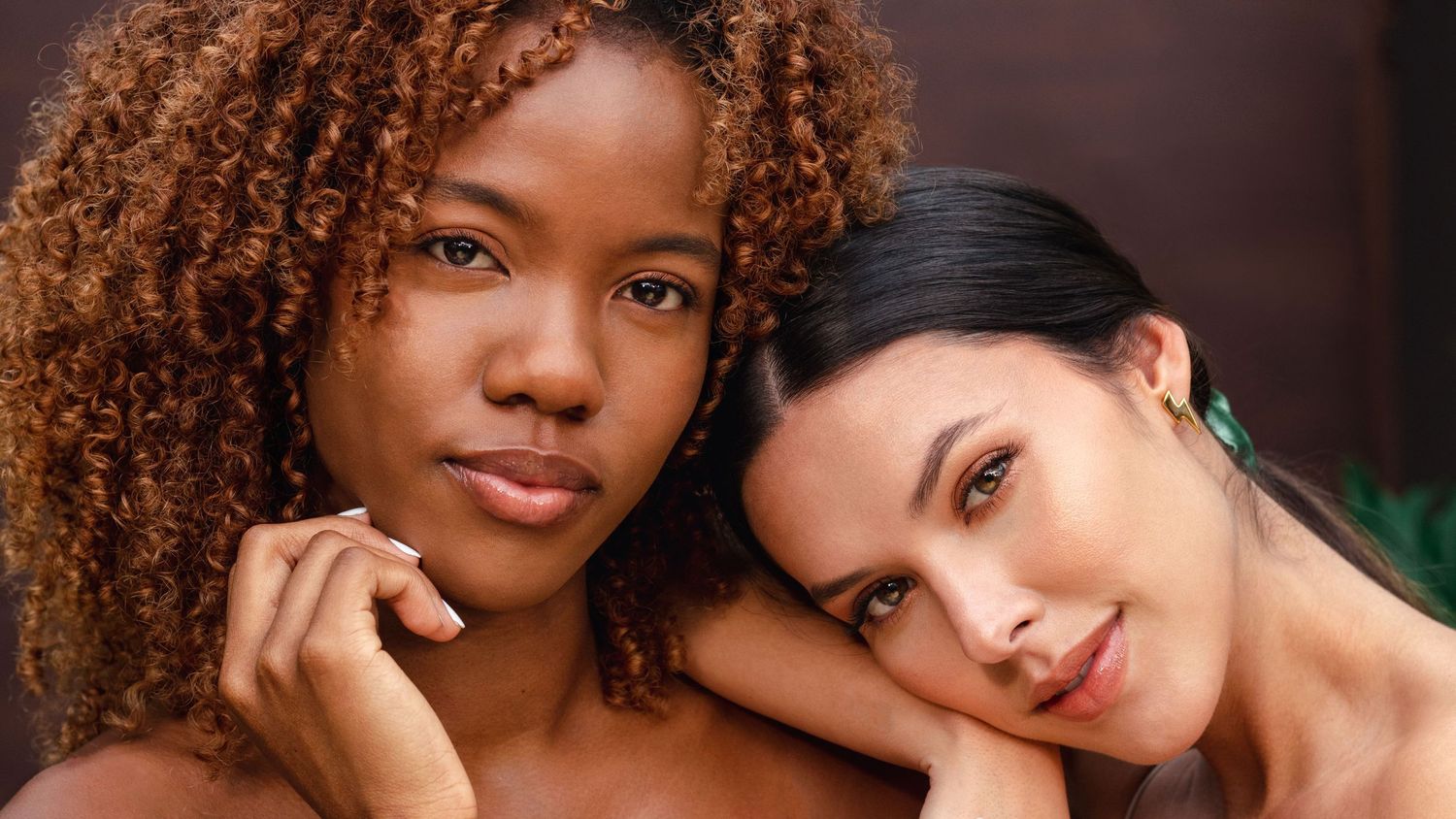 Two friends with different hair textures and skin tones pose together in a warm close-up portrait.