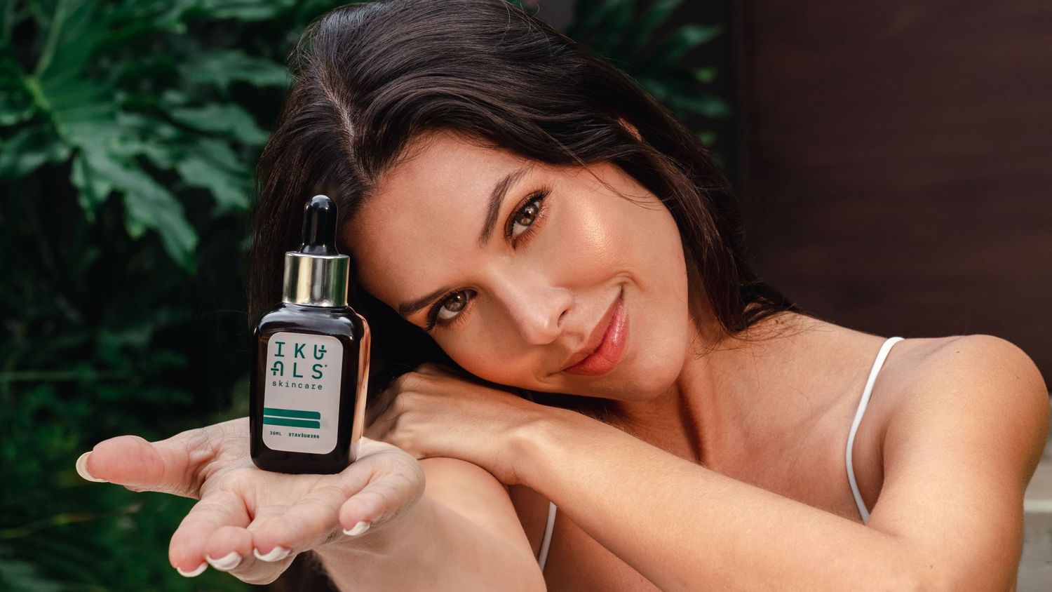 Product photography of a skincare bottle with water splashing in a lush green setting.
