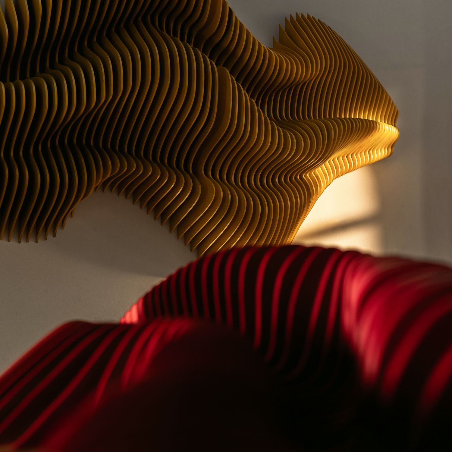 Abstract wavy wall sculpture in yellow and red creating dramatic shadows and patterns.