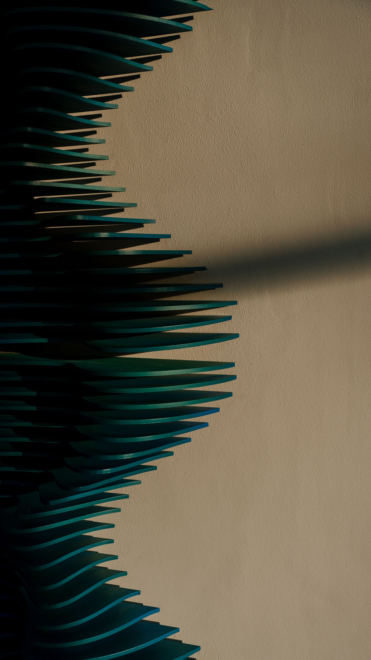 Geometric teal spikes creating rhythmic pattern against beige wall with dramatic shadows.