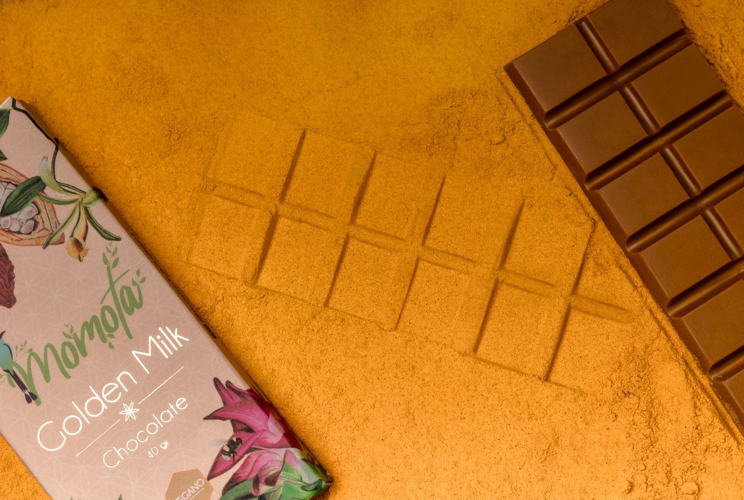 Floral packaging and chocolate bar displayed on textured golden surface.