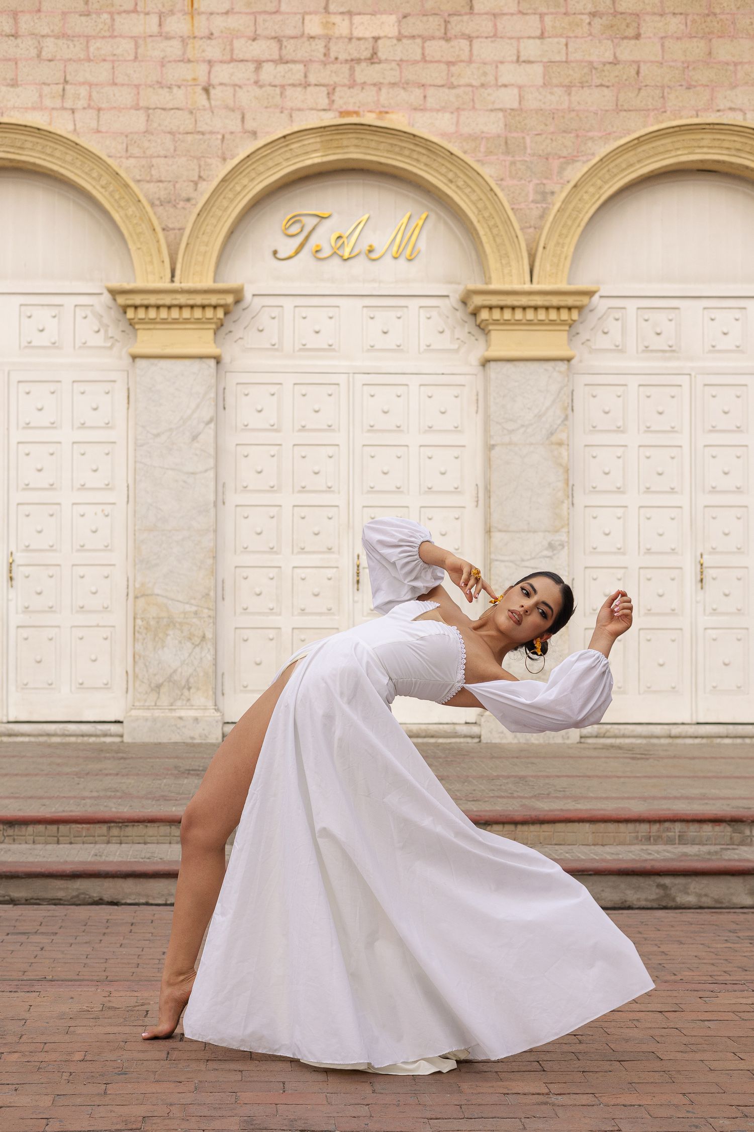 Dancer in flowing white dress performs graceful backbend against architectural arches.