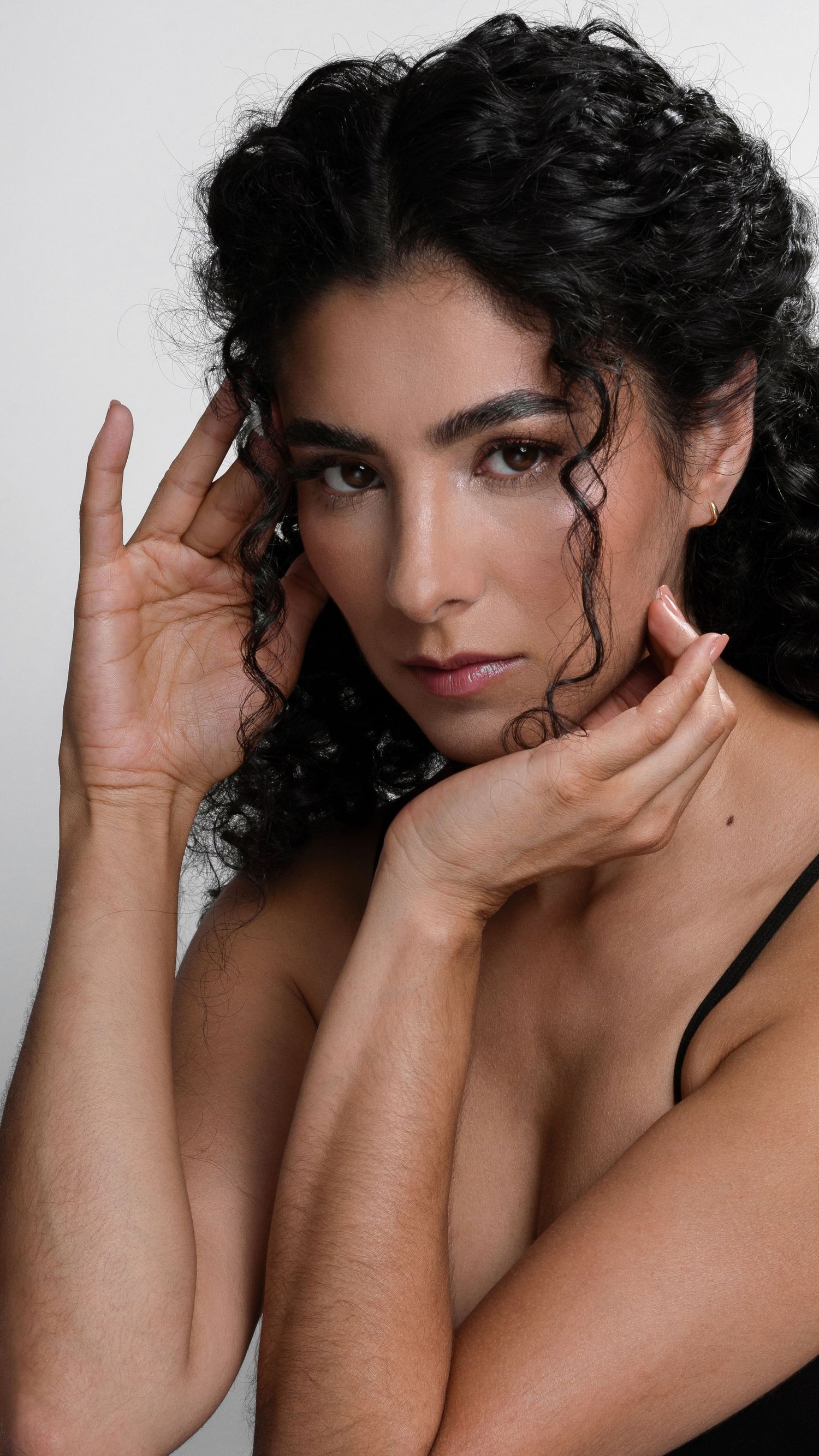 Dramatic beauty portrait with natural curls and delicate hand positioning.