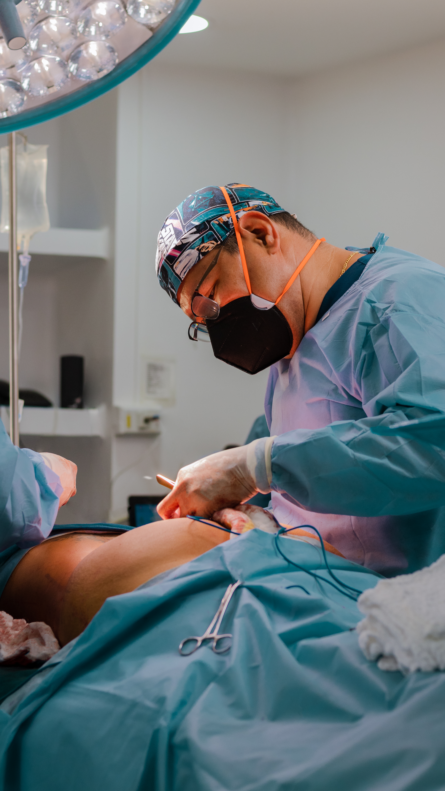 Surgeon performing a medical procedure in an operating room under surgical lights.