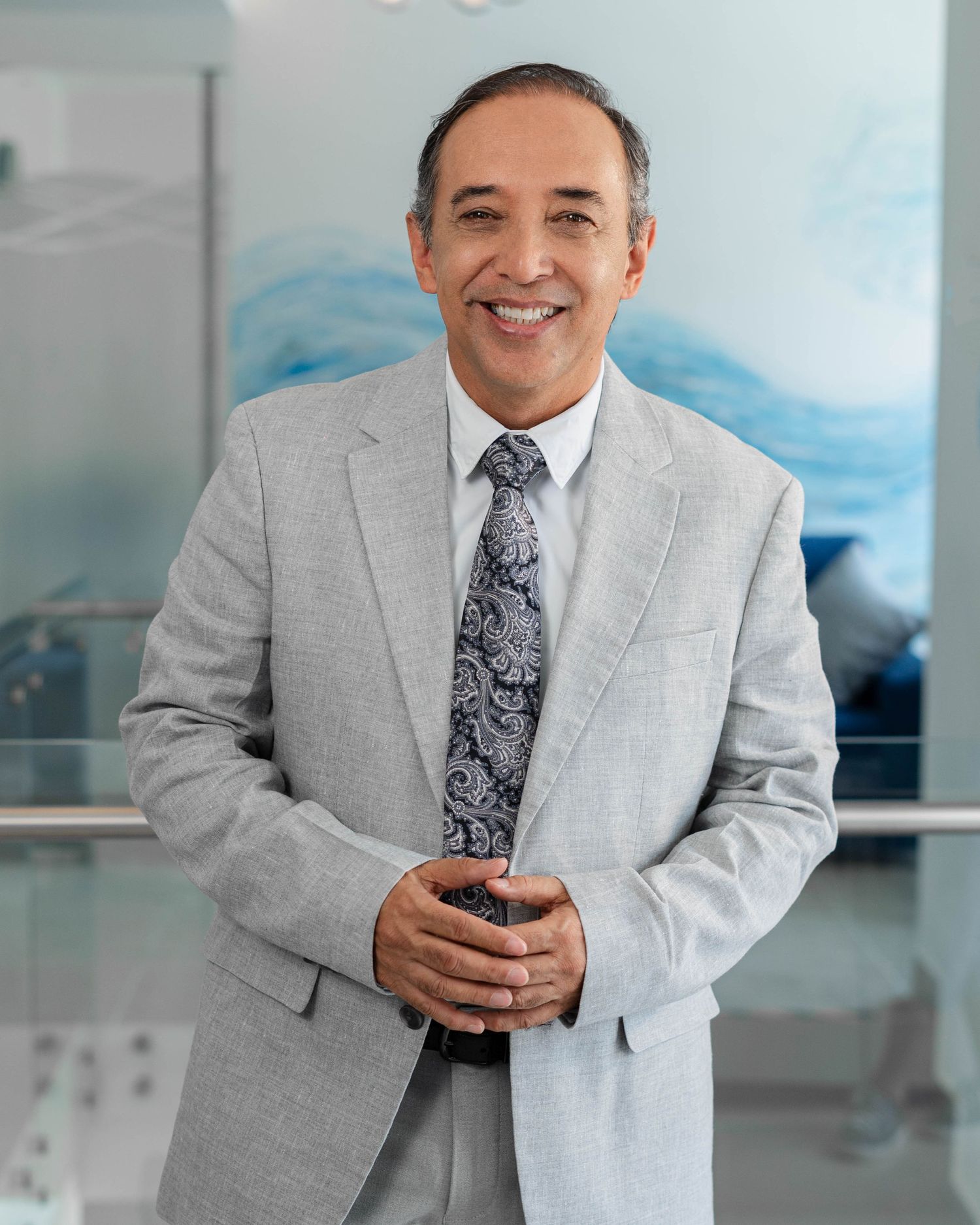 Professional portrait series in light gray suit against blue office background.