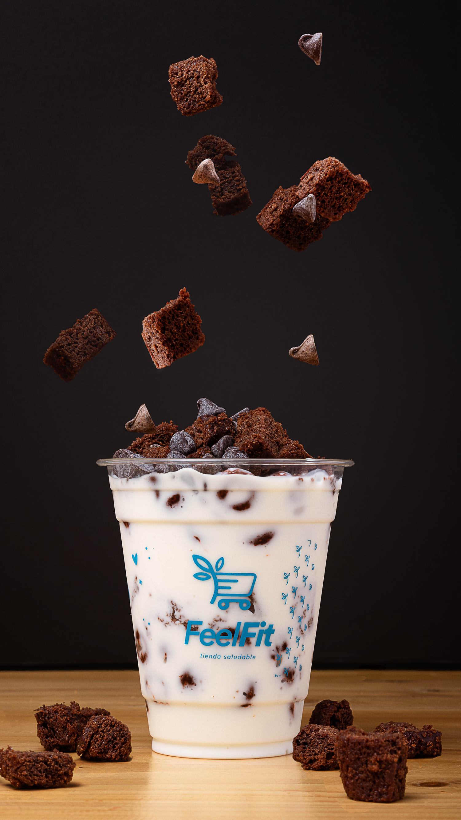 Chocolate brownies falling into a branded milk drink cup on a wooden surface against dark background.