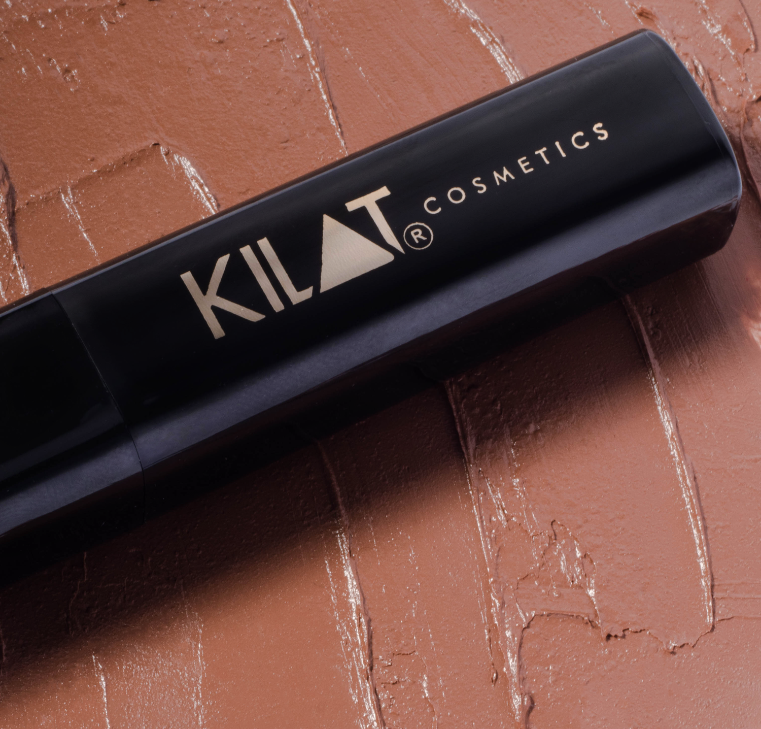 Close up of Kilat Cosmetics black packaging against textured terra cotta background.