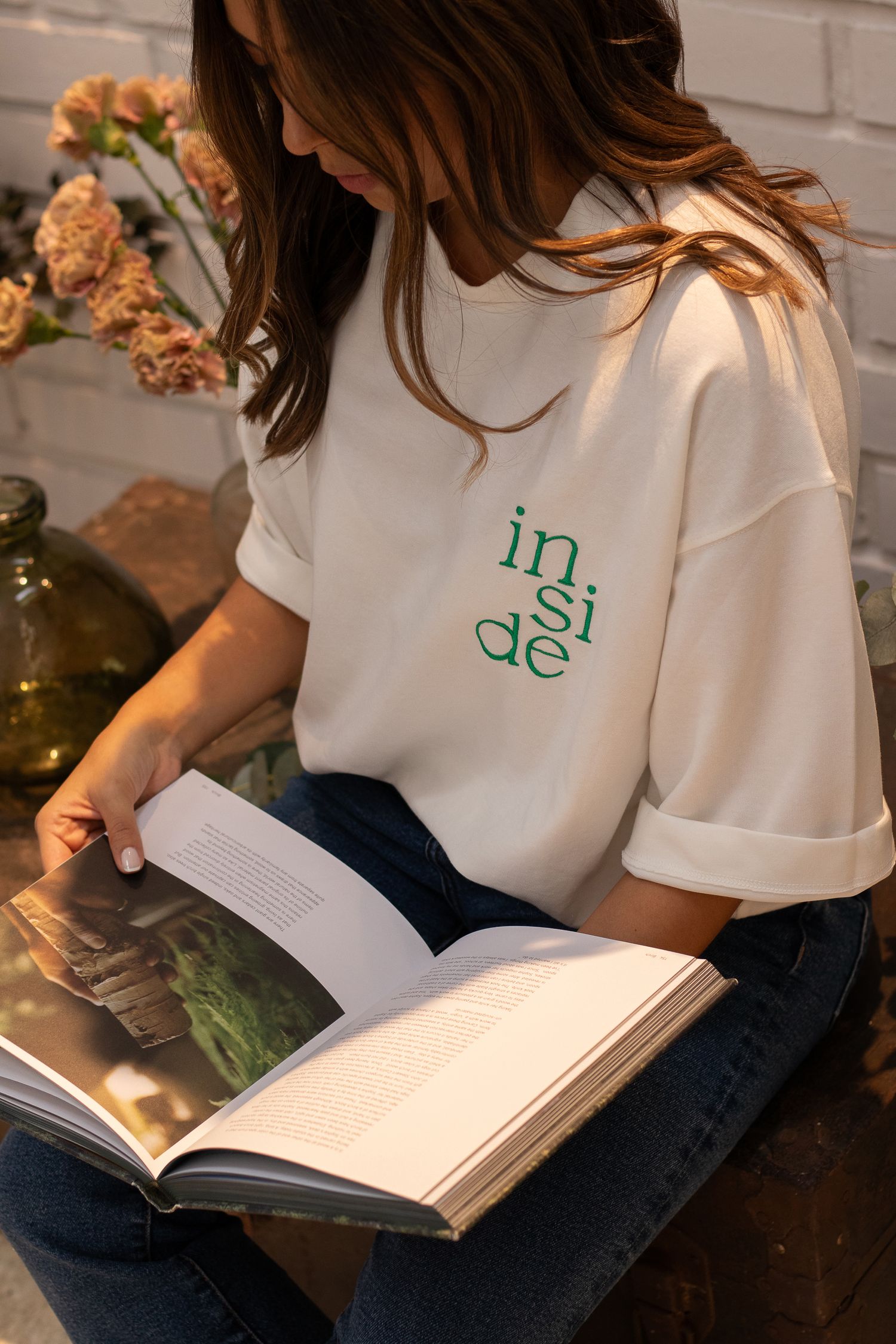 Person reading book while wearing white branded t-shirt with green lettering.