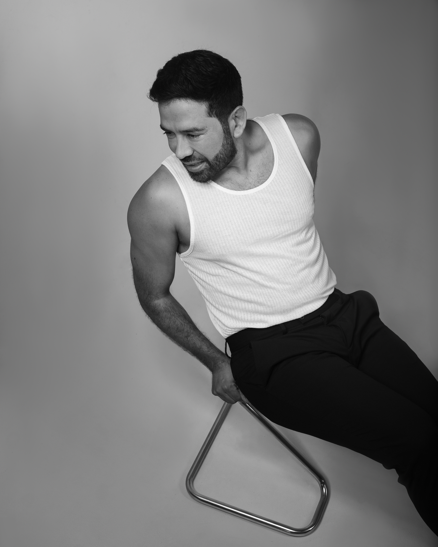 Black and white studio portrait of performer seated on modern chair.
