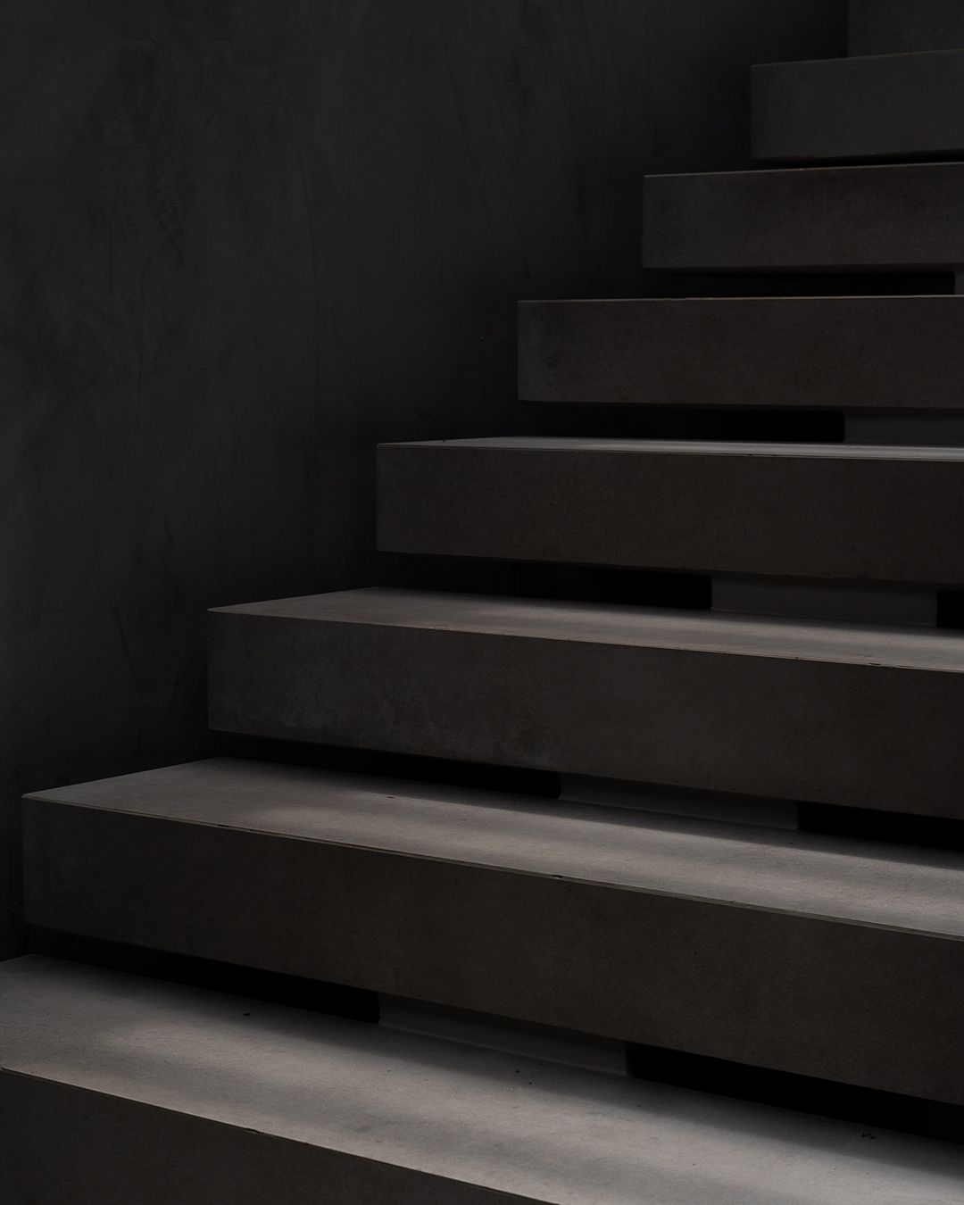 Dark concrete staircase with minimalist geometric design and strong shadows.