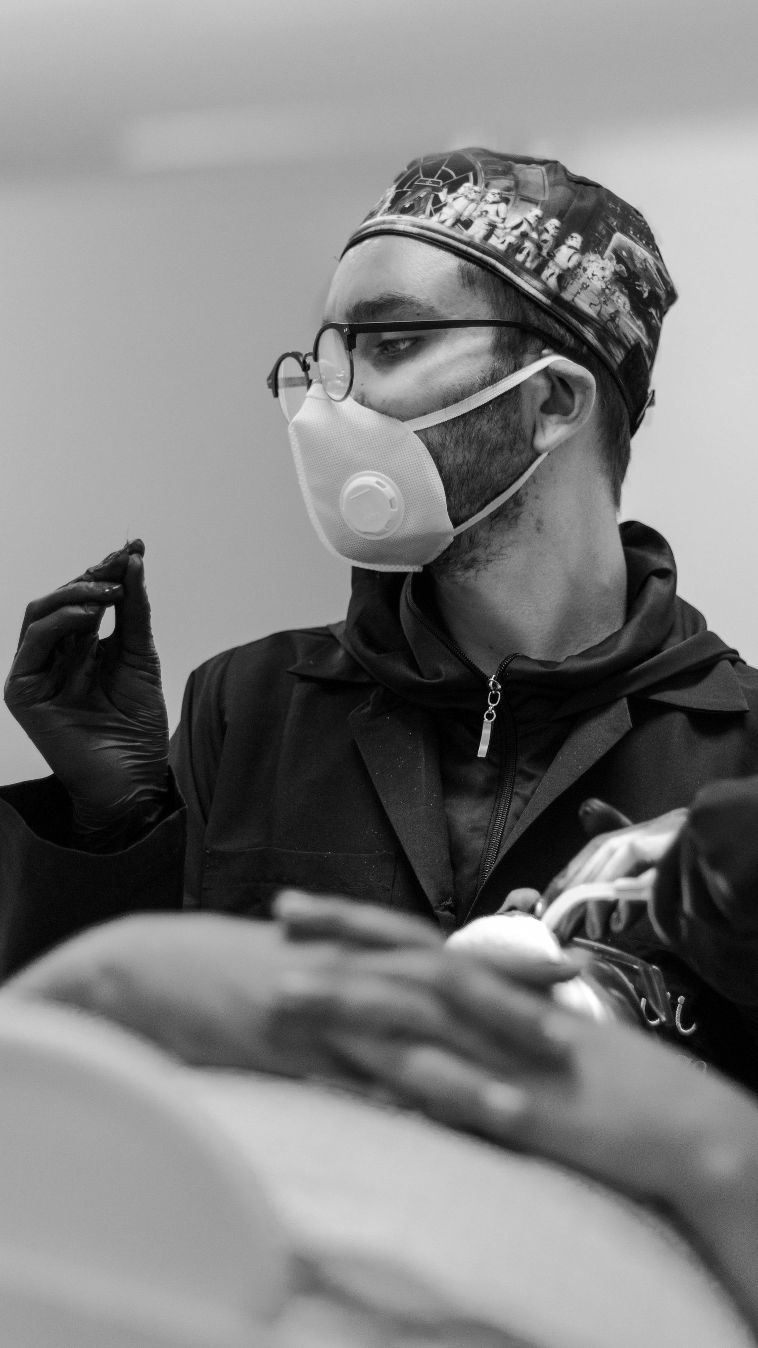 Medical professional wearing protective mask and surgical cap during procedure.