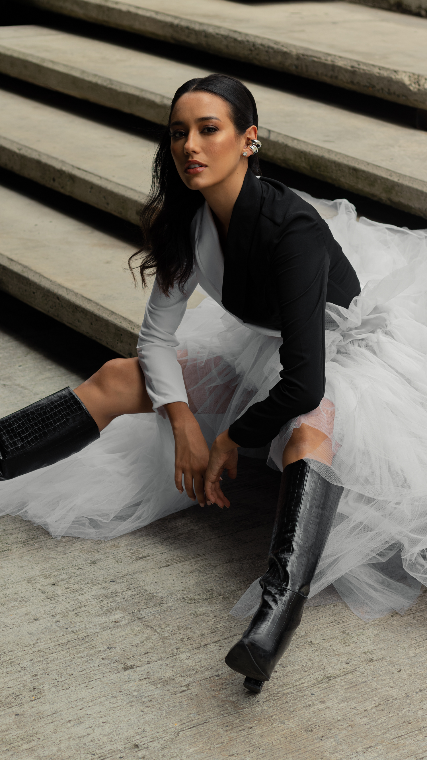 Dramatic contrast of black blazer and white tulle skirt with leather boots on concrete steps.