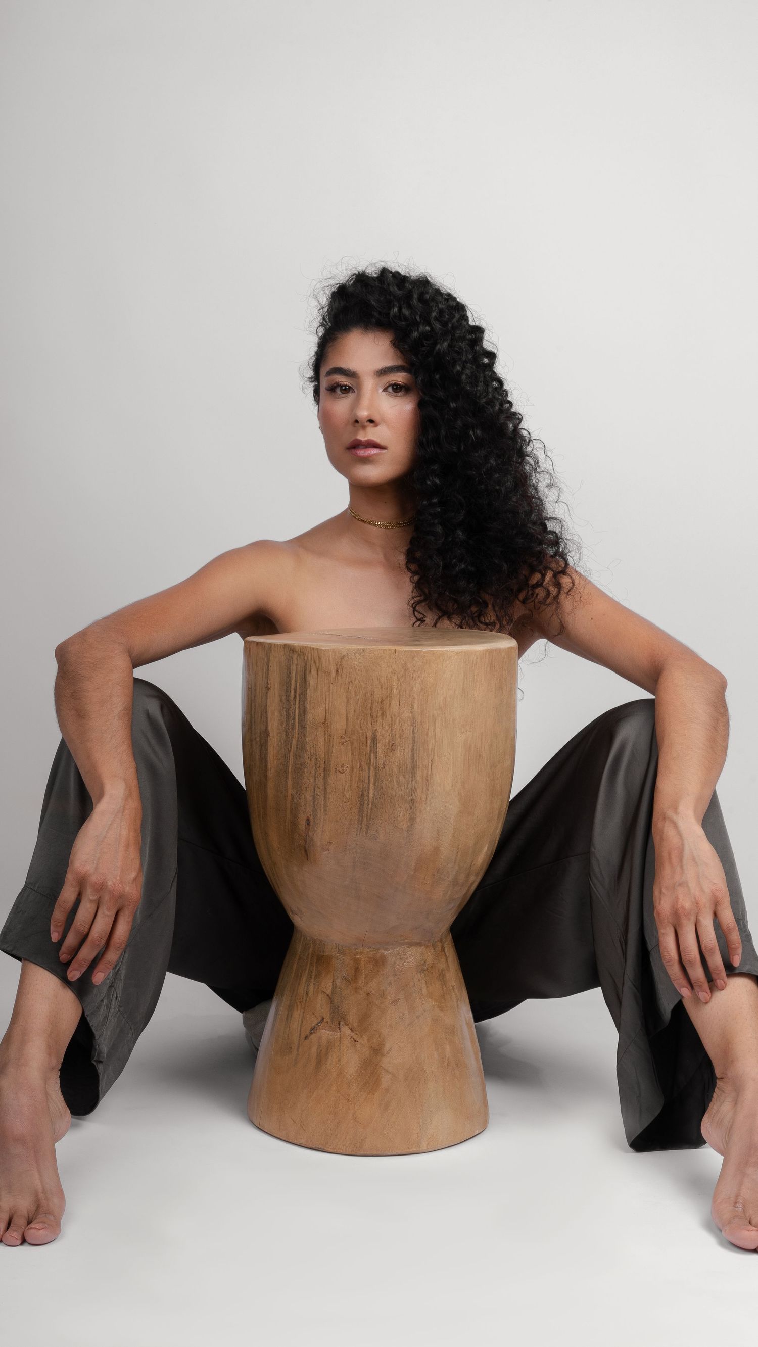 Artistic fashion photo with model seated on wooden stool wearing flowing pants.
