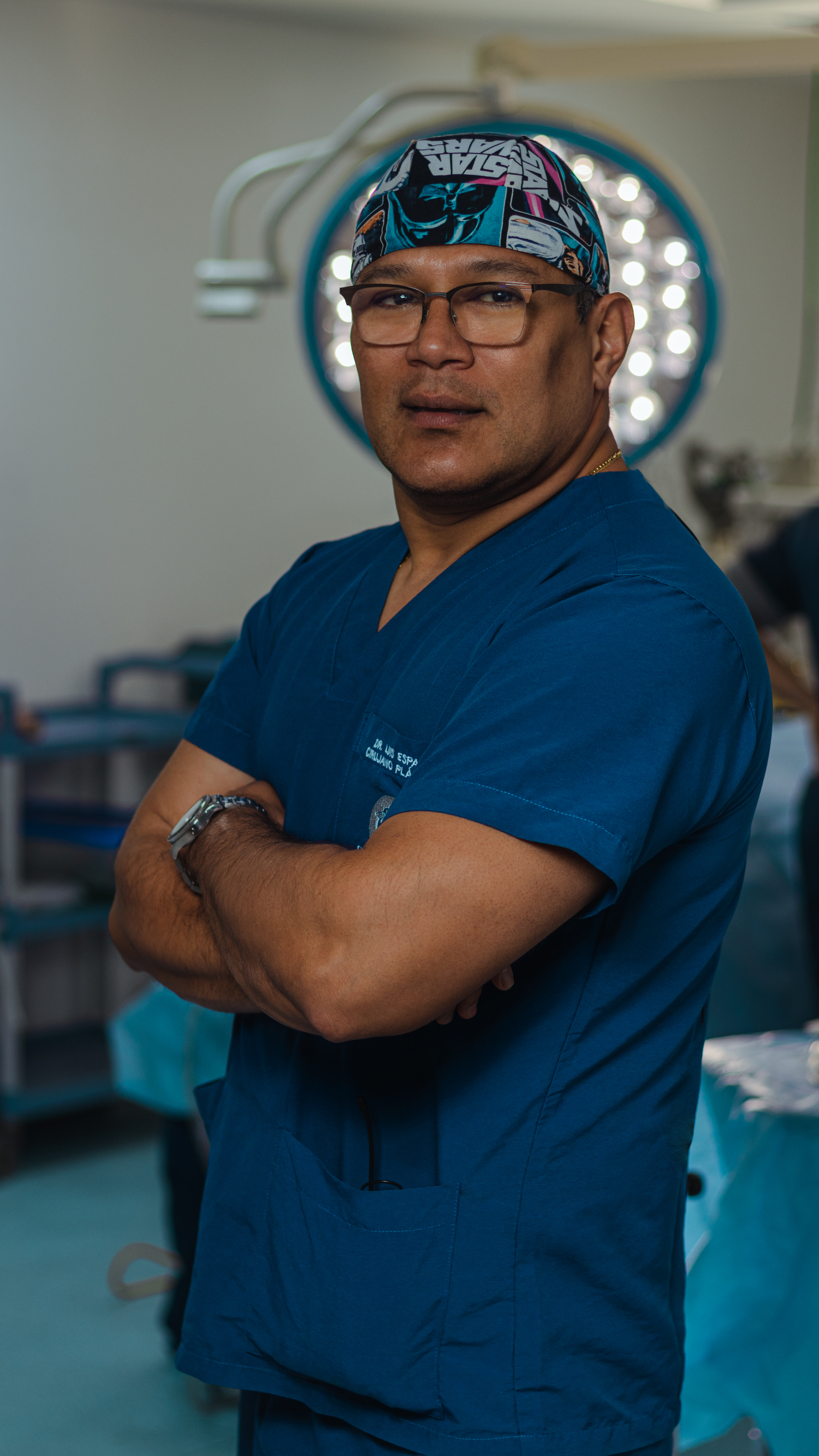 Medical professional in blue scrubs and surgical cap standing in operating room.