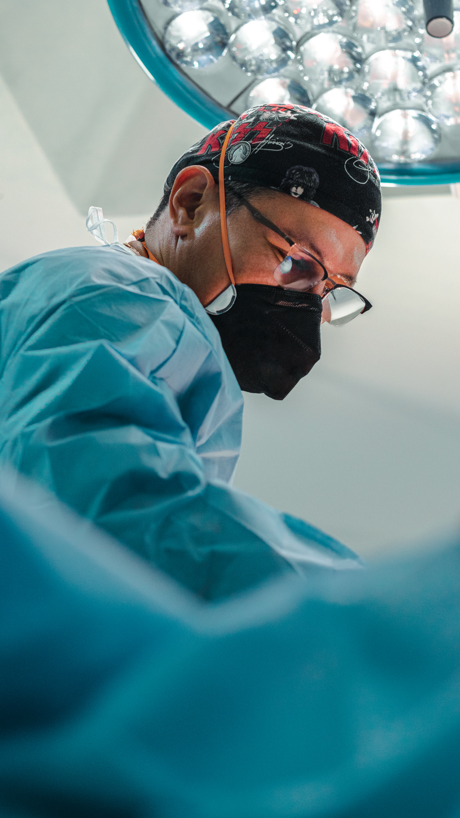 Surgeon in scrubs and mask concentrates during operation under surgical lighting.