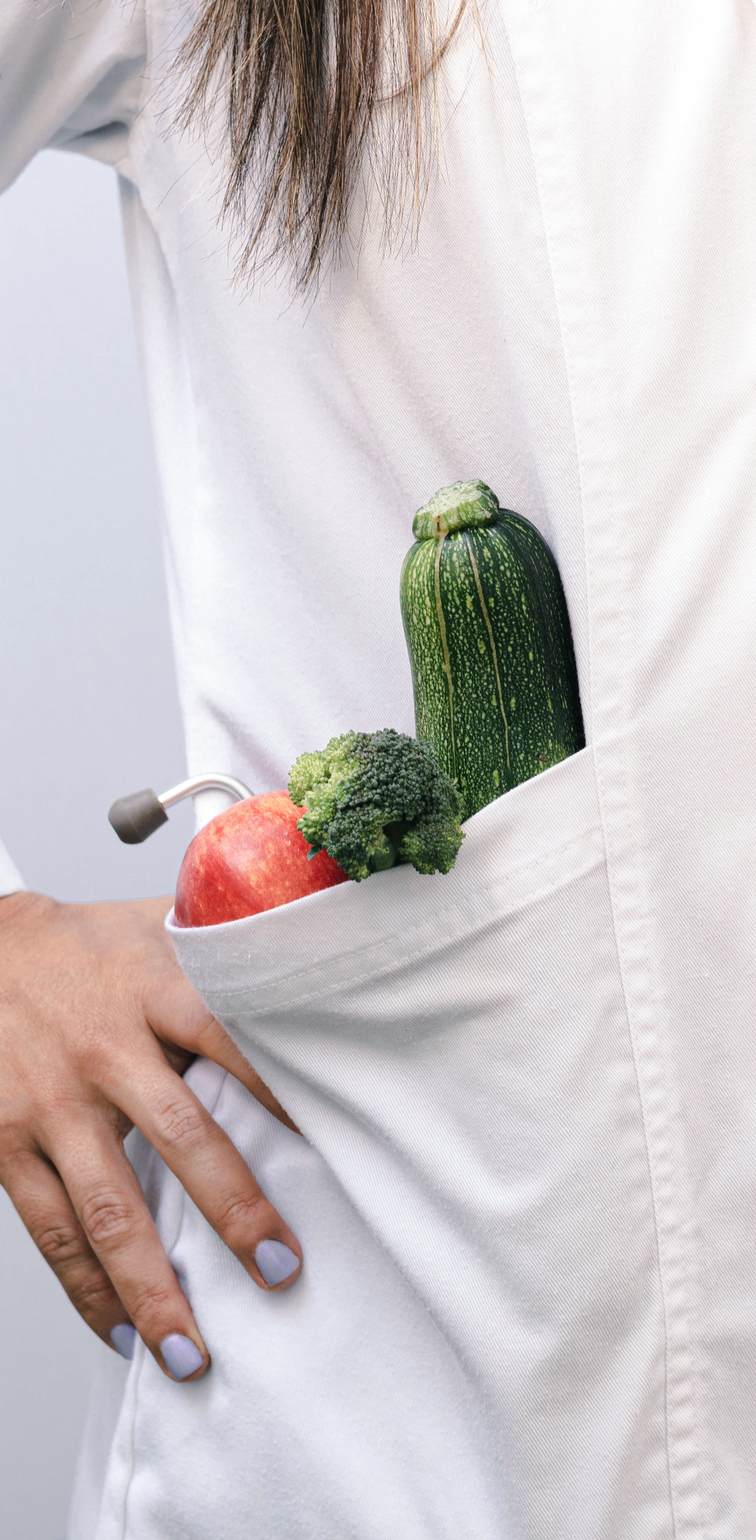 Fresh vegetables and apple tucked into the pocket of a white coat, suggesting healthy eating habits.