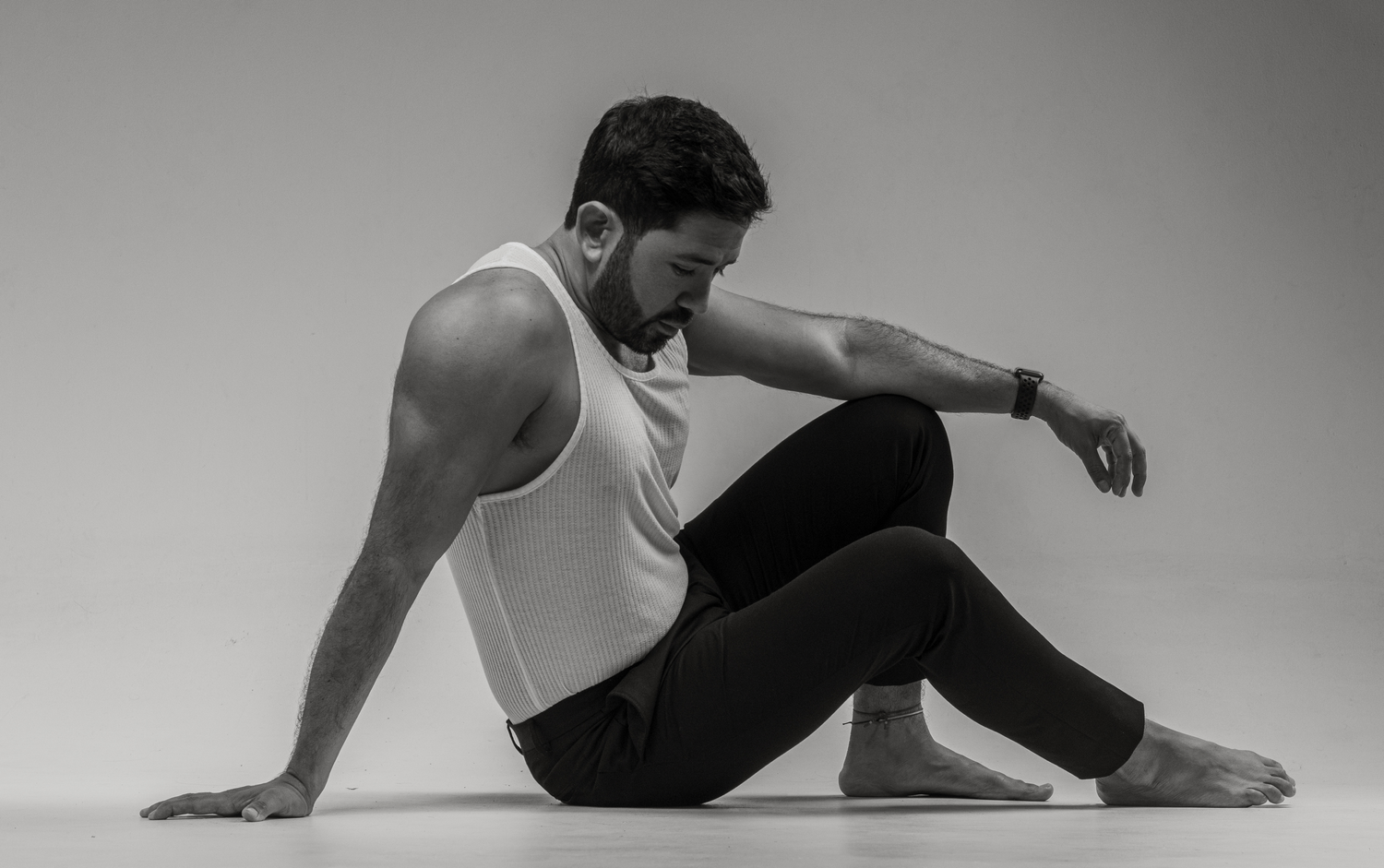 Artistic black and white portrait of dancer in white tank top performing floor movement.