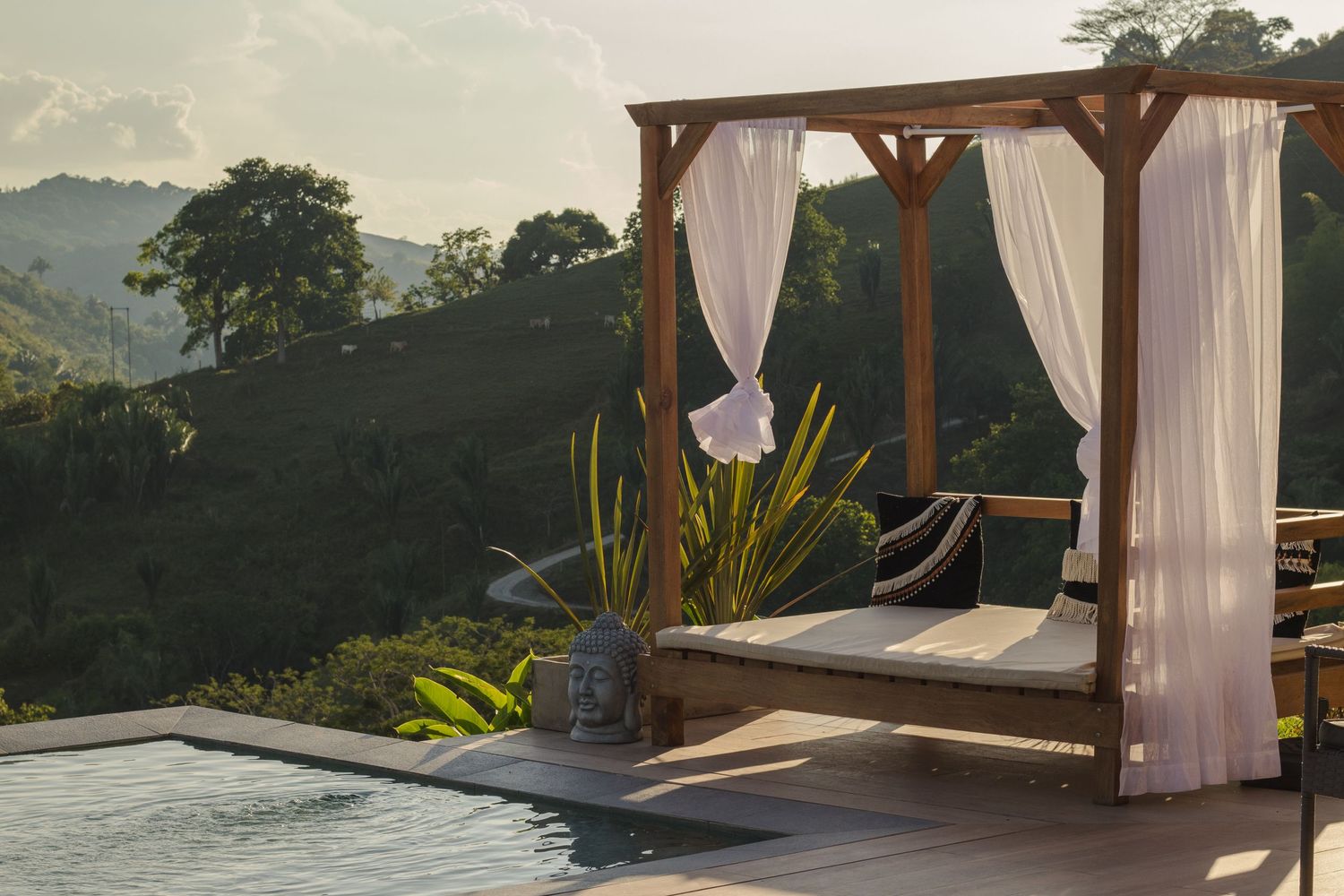 Luxury poolside cabana with flowing white curtains against mountainous landscape at golden hour.
