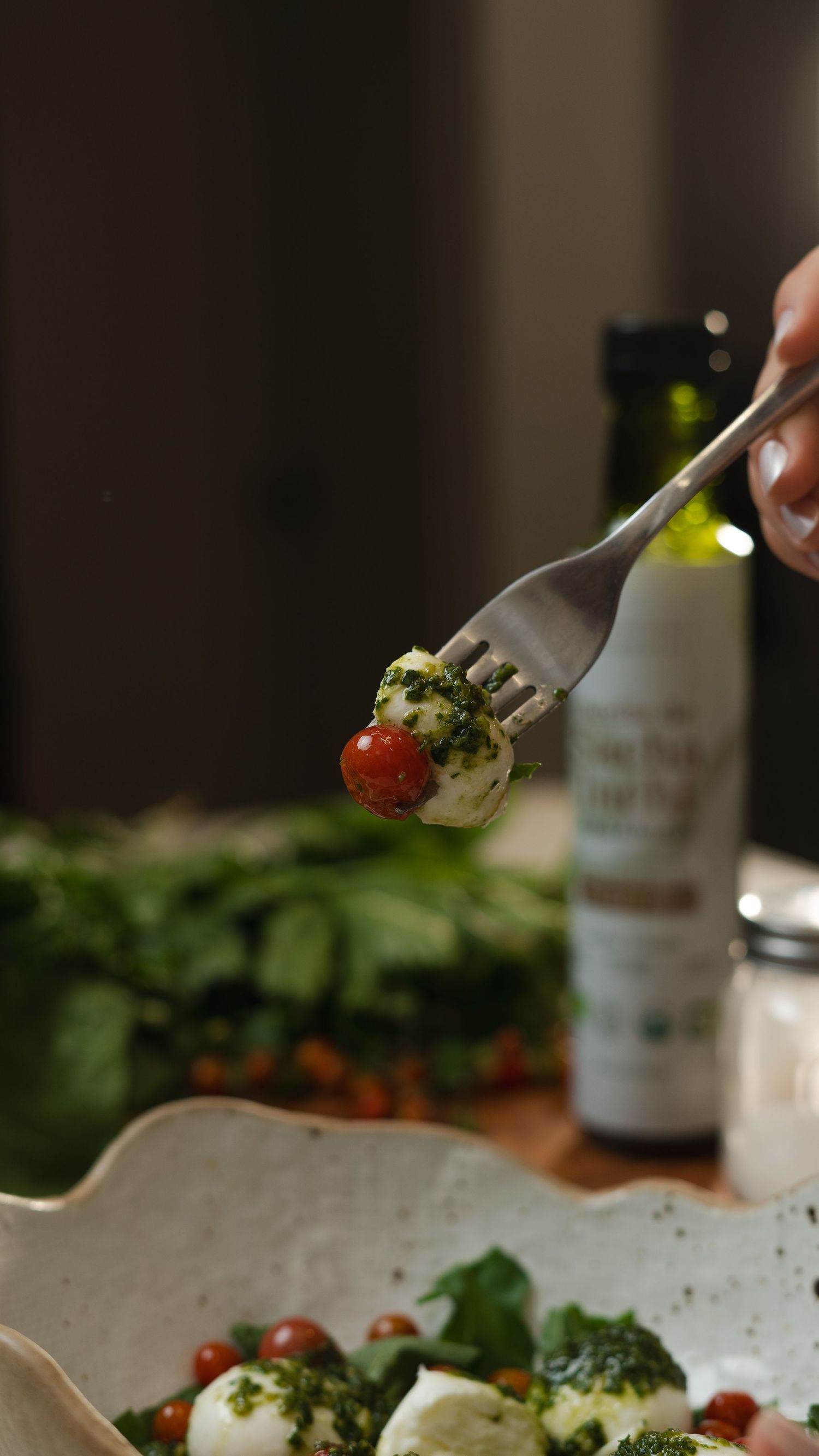 A fork lifts a cherry tomato and mozzarella appetizer drizzled with herbs.