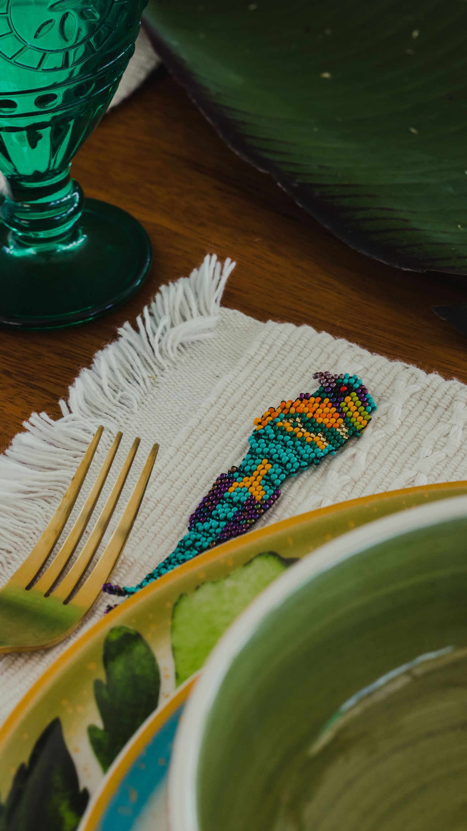 Elegant table setting with emerald glassware, gold cutlery, and colorful beaded details.