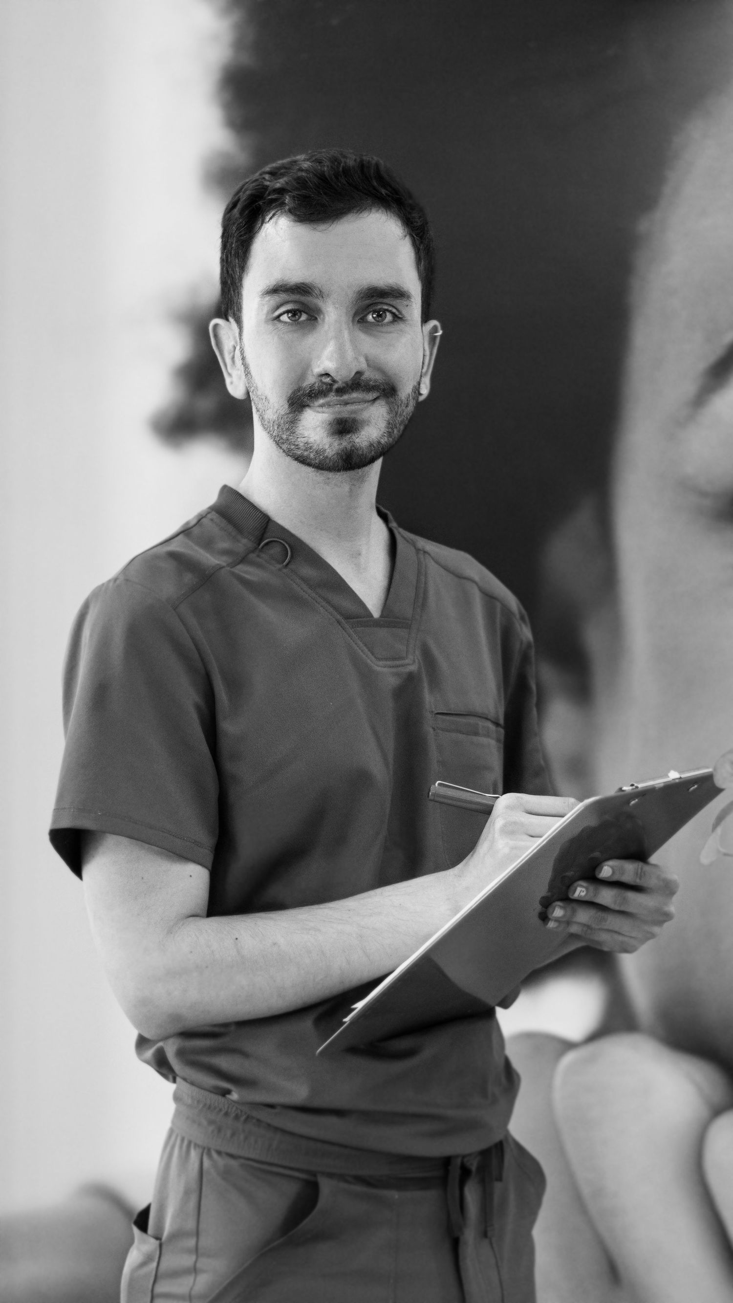 Healthcare professional in scrubs holding clipboard against neutral background.
