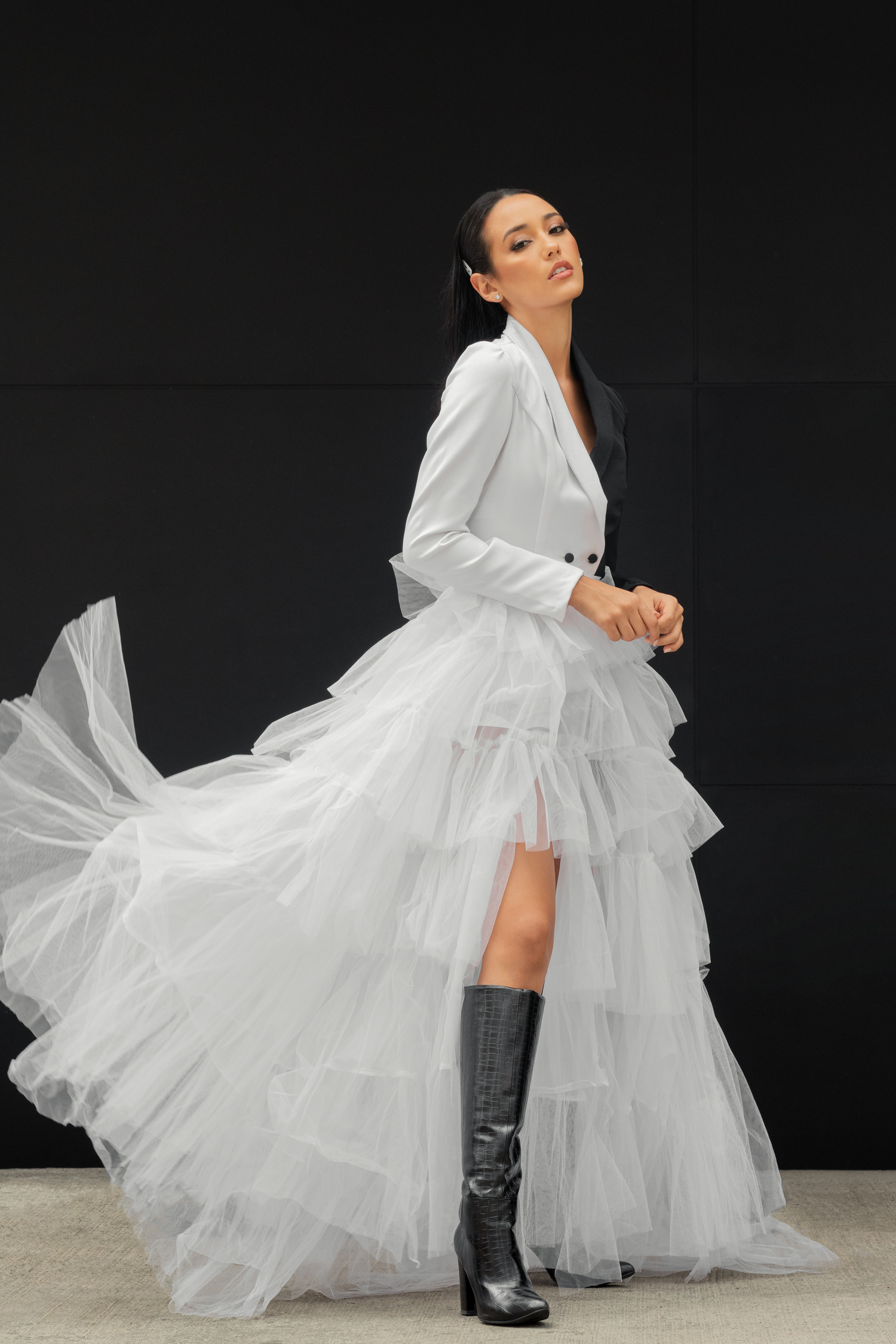 Dramatic fashion shot of white tulle gown with black boots against dark background.