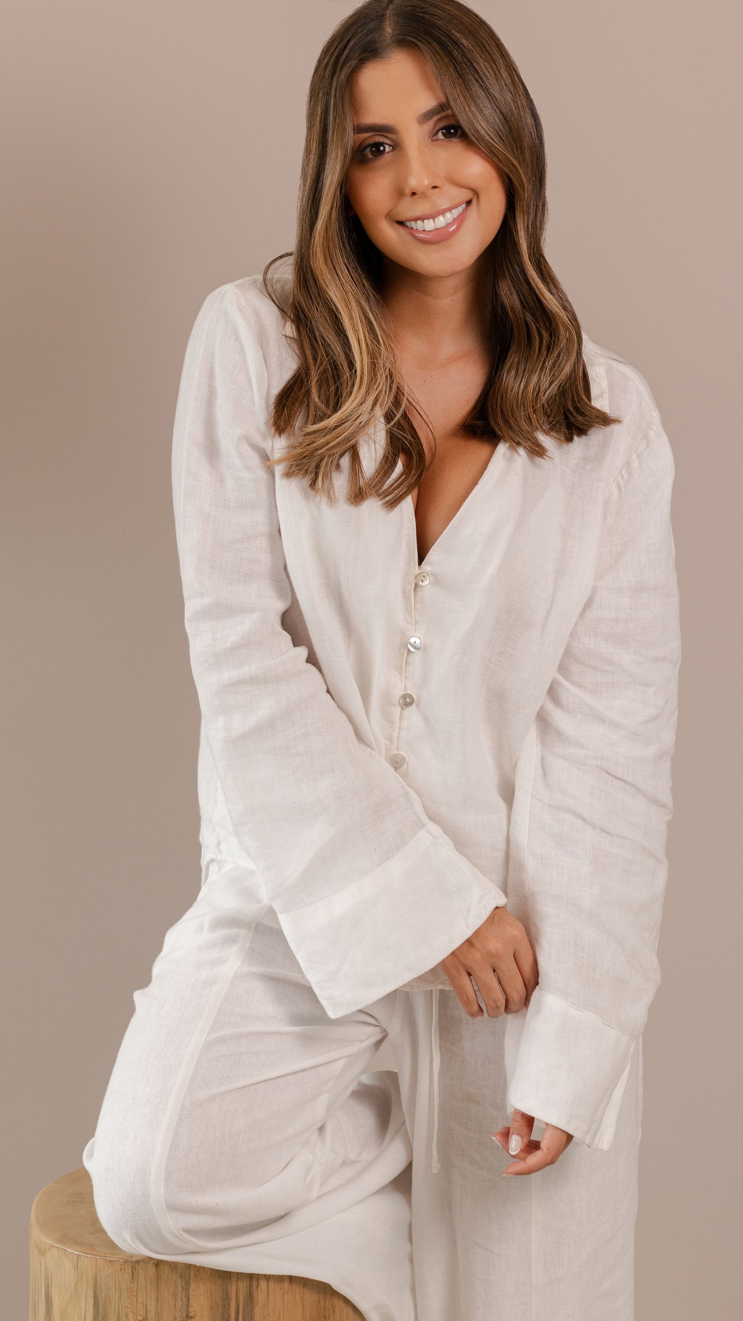Lifestyle photo of person wearing white linen loungewear sitting on wooden stool.