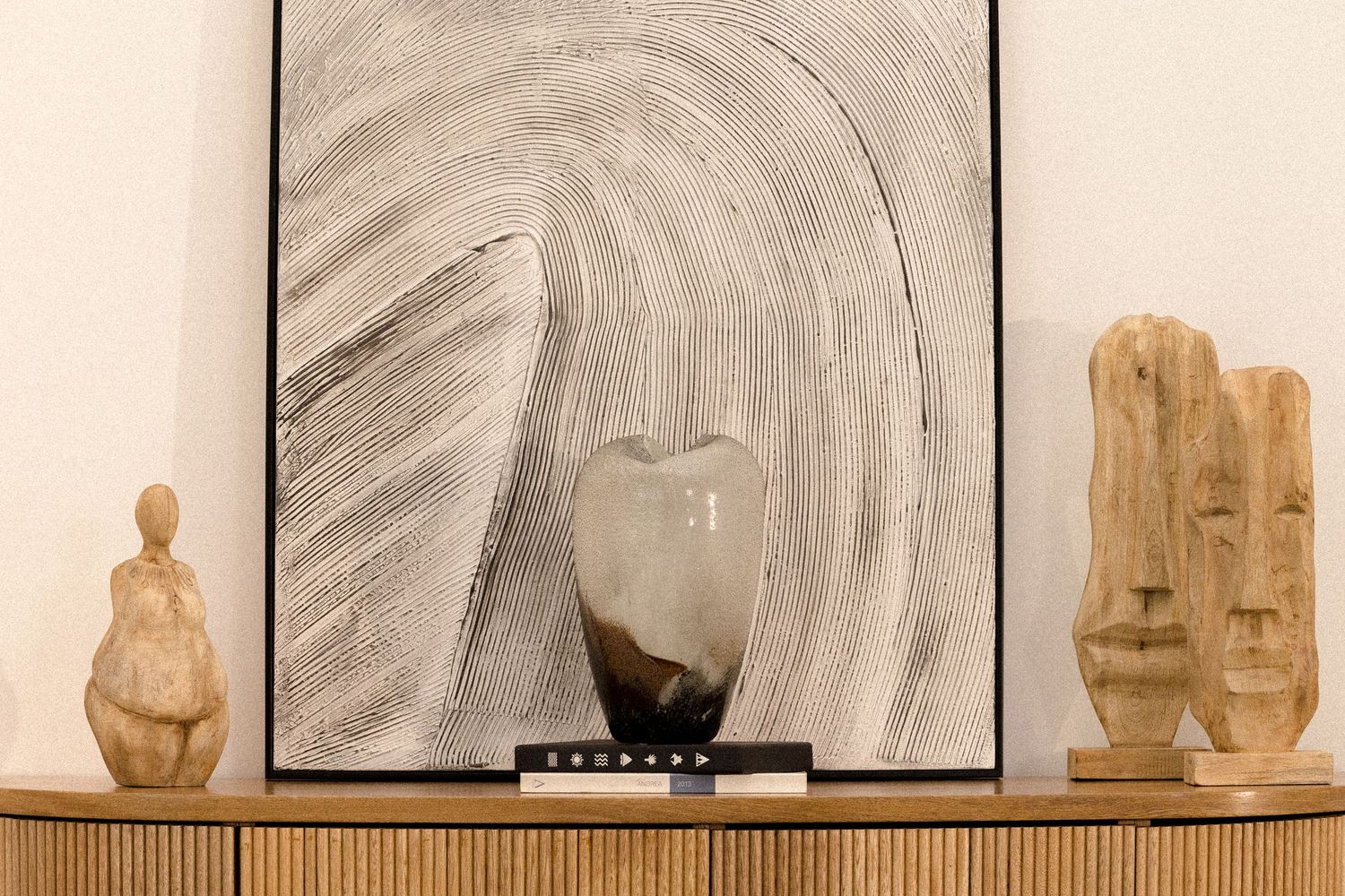Collection of wooden sculptures displayed against abstract swirling artwork in neutral tones.