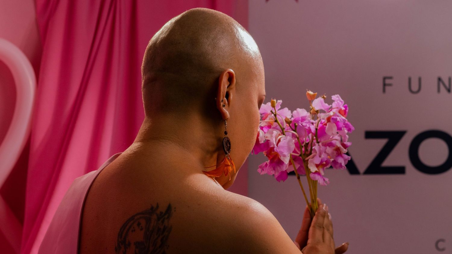 Person holding pink orchid flowers against a pink background in artistic lighting.