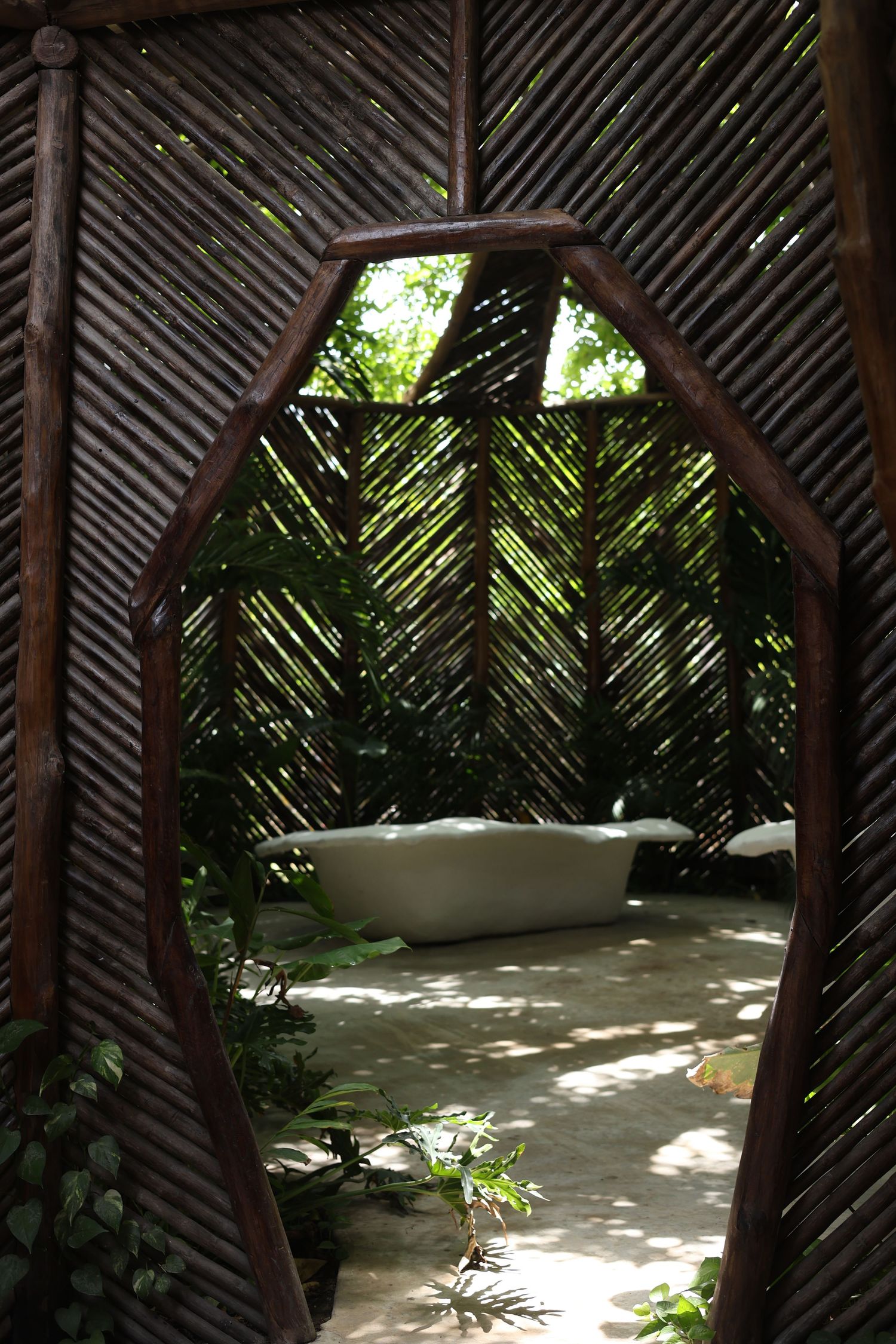 Outdoor bathtub viewed through wooden archway surrounded by tropical palm fronds.
