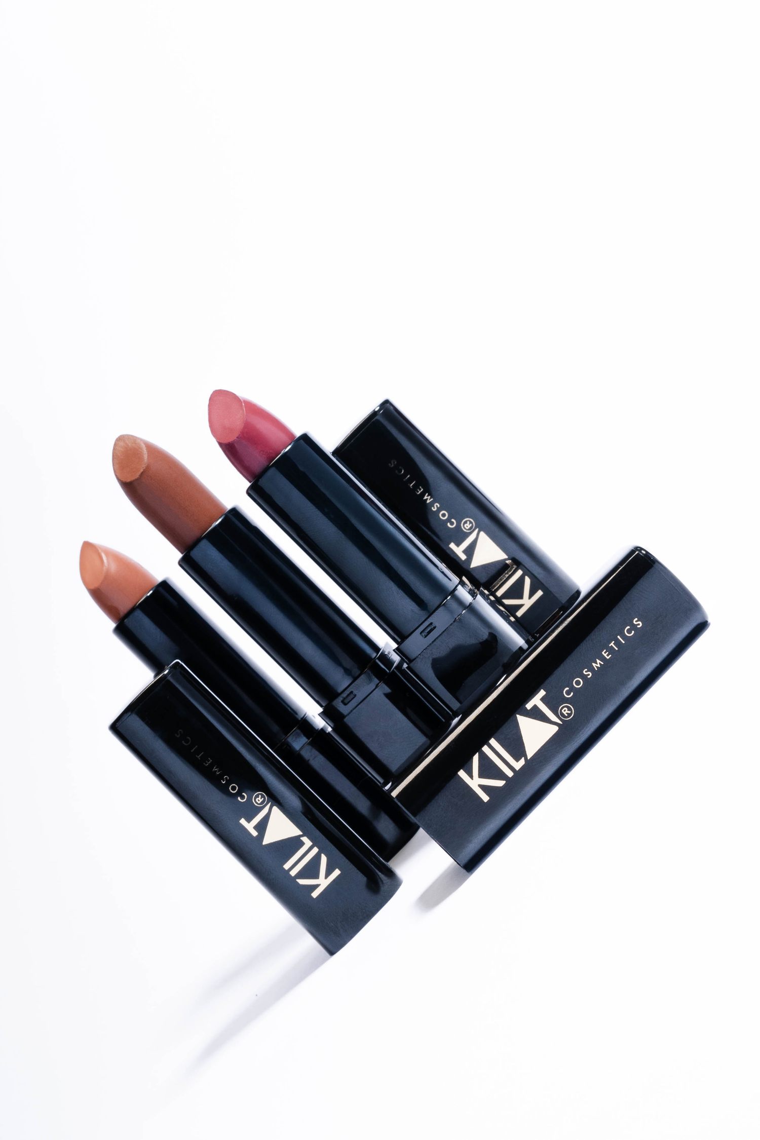 Collection of nude and pink lipsticks from Kilat Cosmetics arranged on white background.