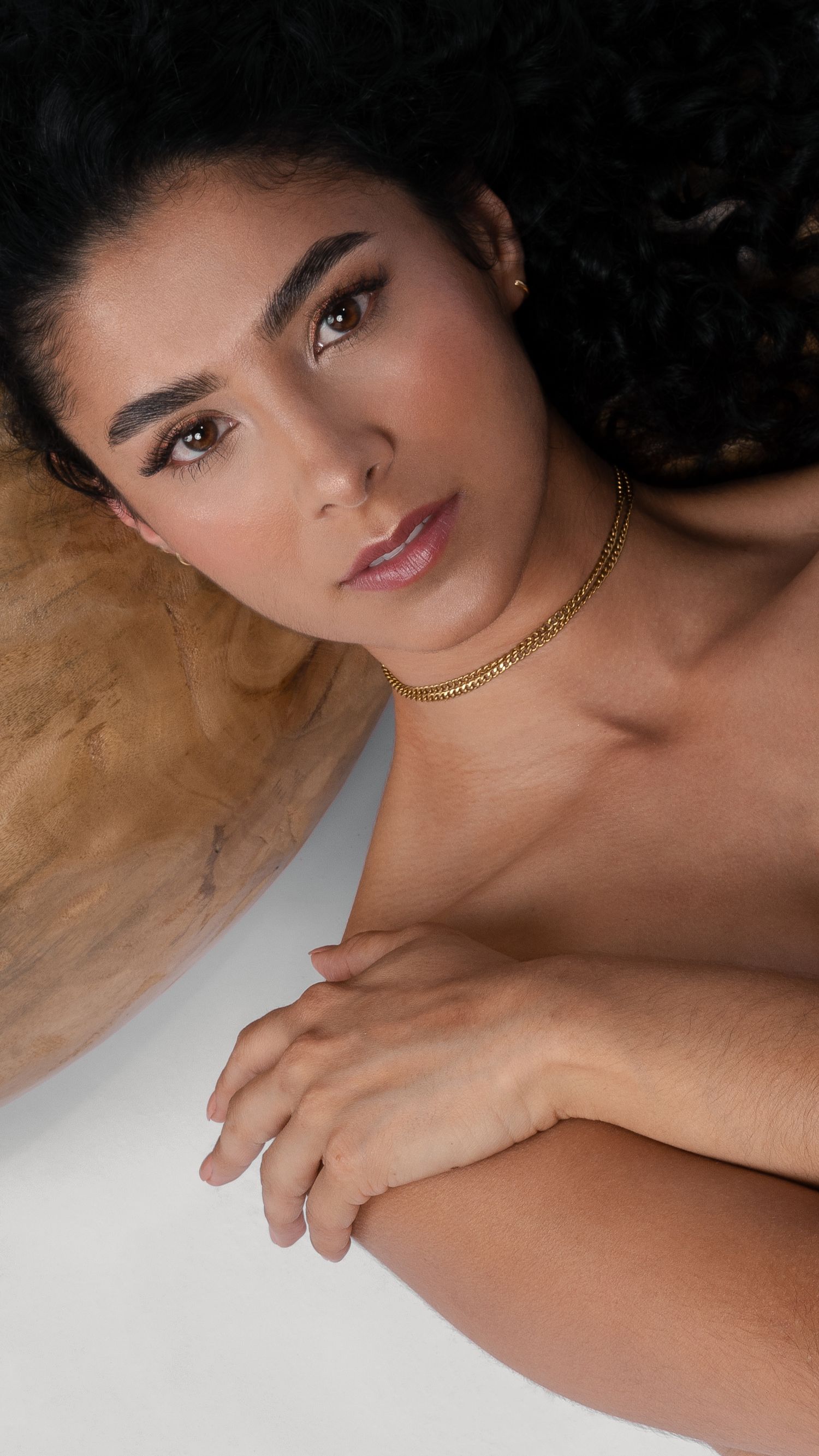 Beauty portrait featuring gold chain necklace and natural makeup against beige backdrop.