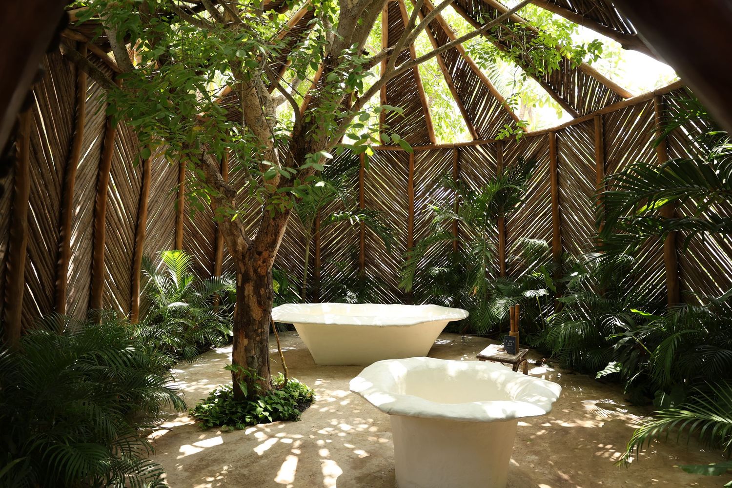 Luxurious outdoor bathtub surrounded by tropical palm fronds and bamboo walls creating a spa-like sanctuary.